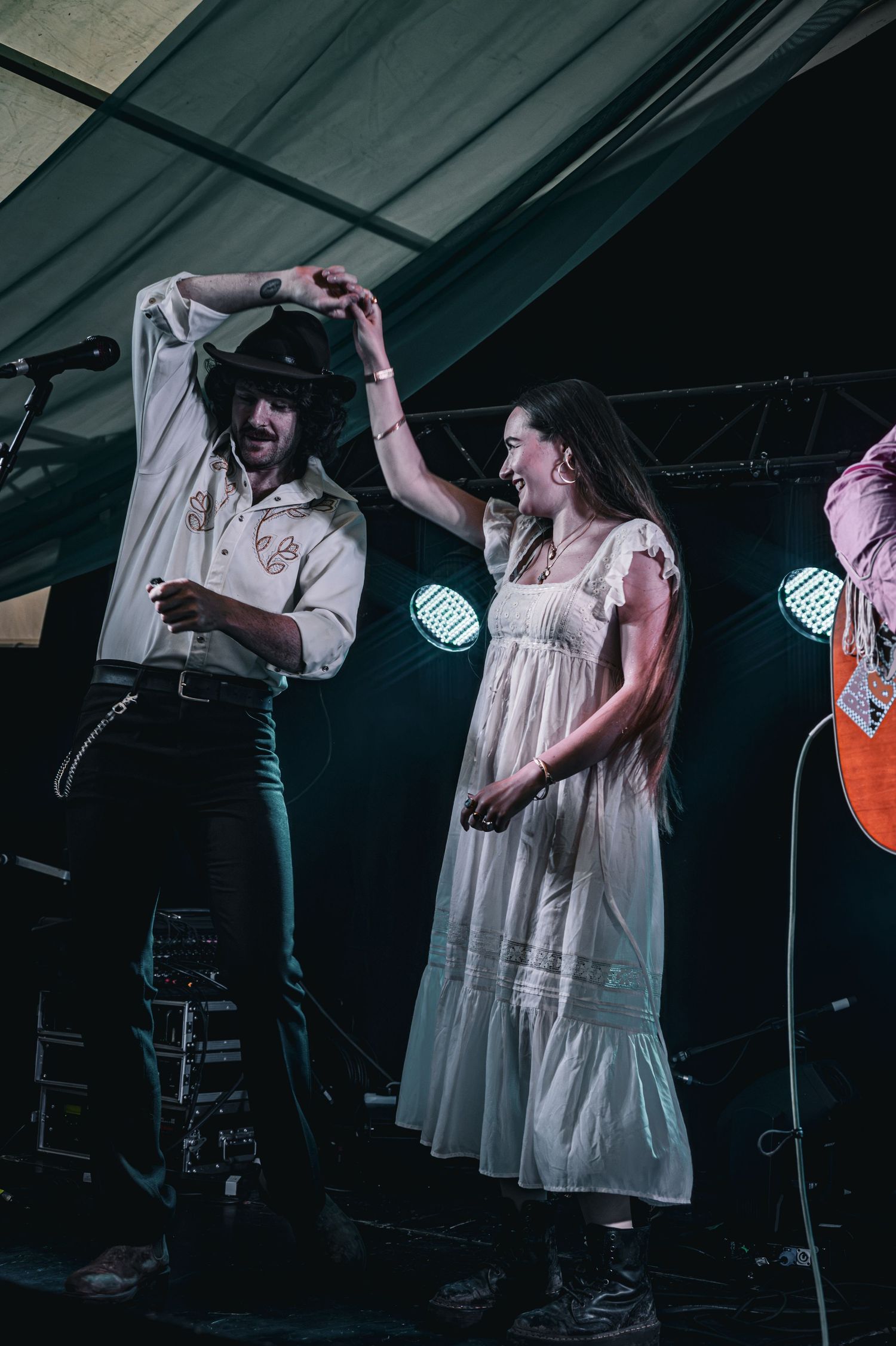 A man in a cowboy hat and woman in a white dress dance together on a concert stage with colorful lights.