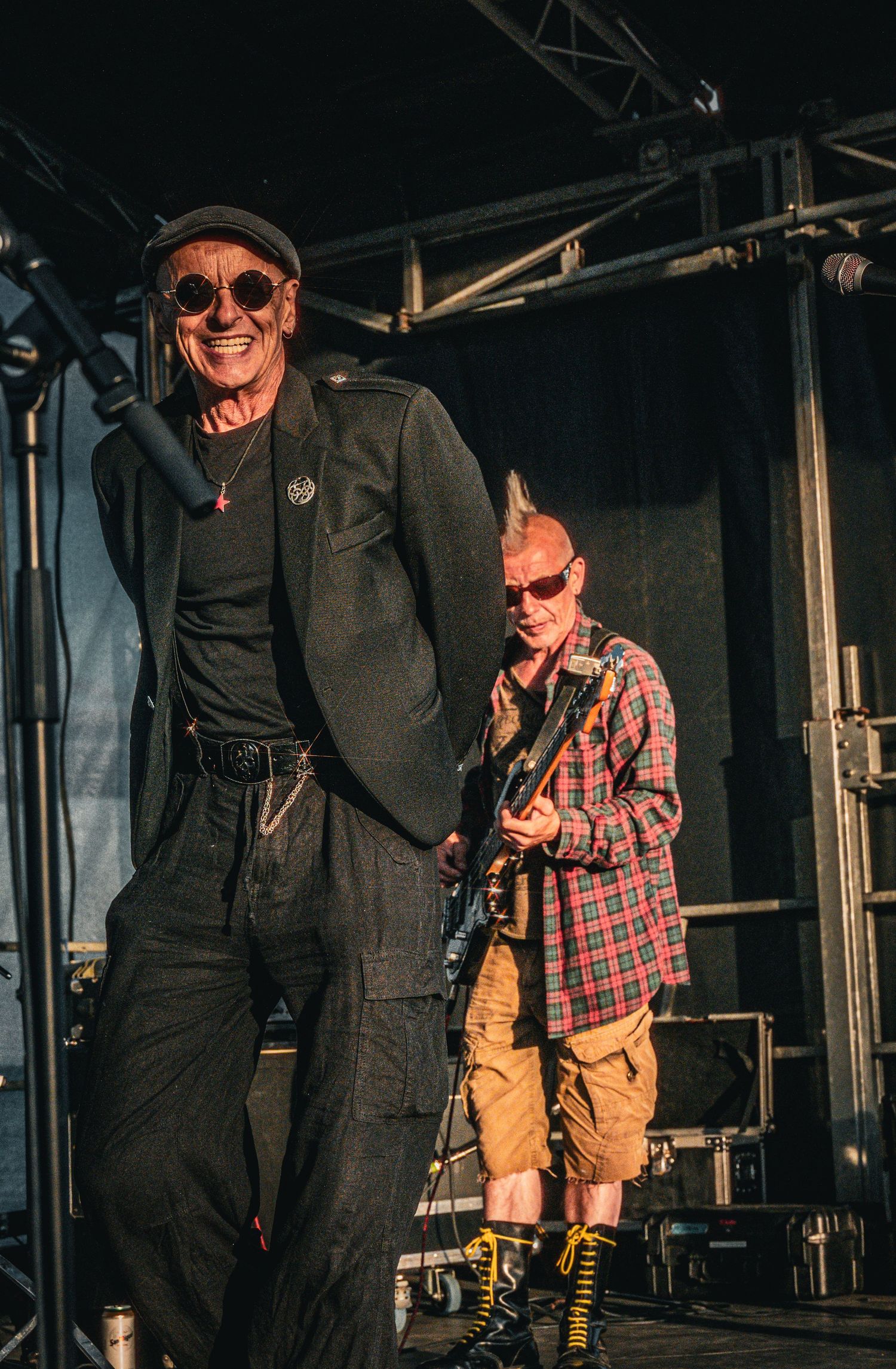 Two rock performers on stage, singer in black and guitarist in plaid shirt with mohawk hairstyle.