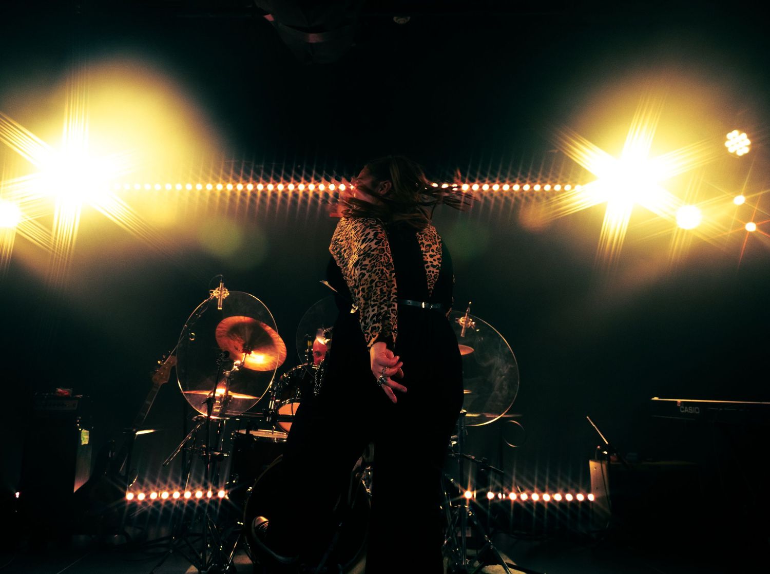 A silhouetted performer stands on stage backlit by bright spotlights creating dramatic lens flare effects.