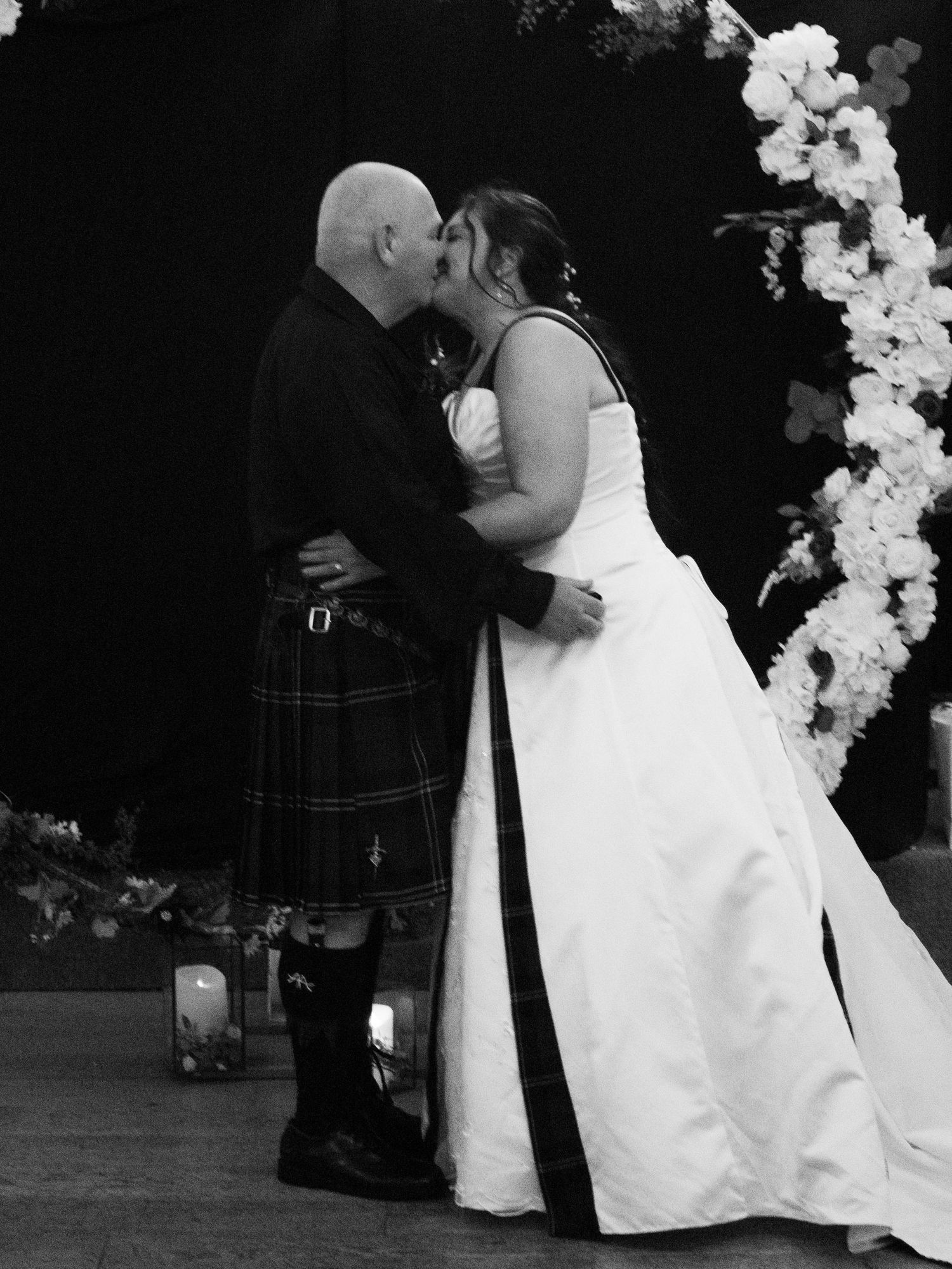 Bride and groom sharing a kiss at the altar, groom wearing a traditional Scottish kilt, bride in a white gown.