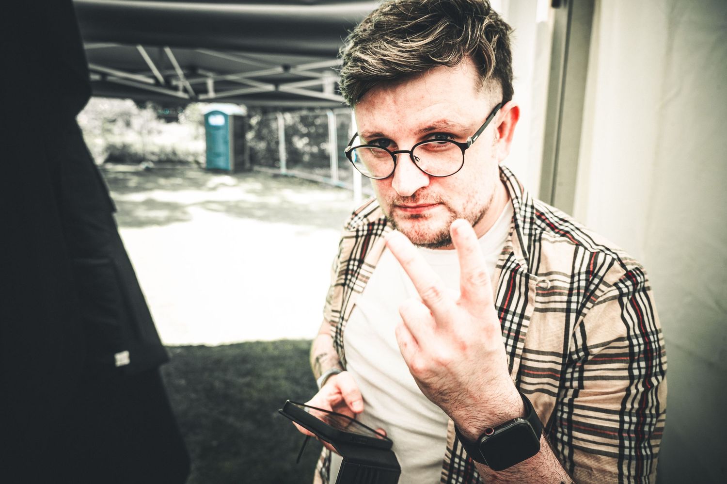 Young man in plaid shirt wearing glasses looking at smartphone outdoors.