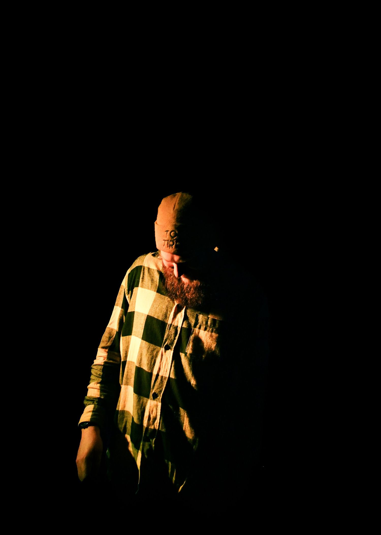 A silhouetted figure in a checkered shirt stands against a dark background with dramatic lighting.