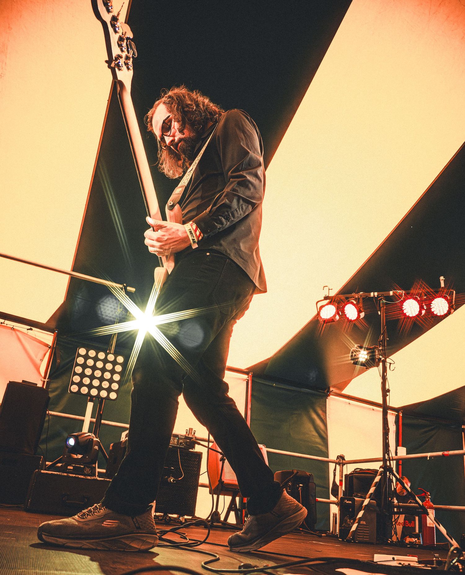 Guitarist performing on stage with dramatic lighting, playing electric guitar with intense energy at an outdoor music festival.