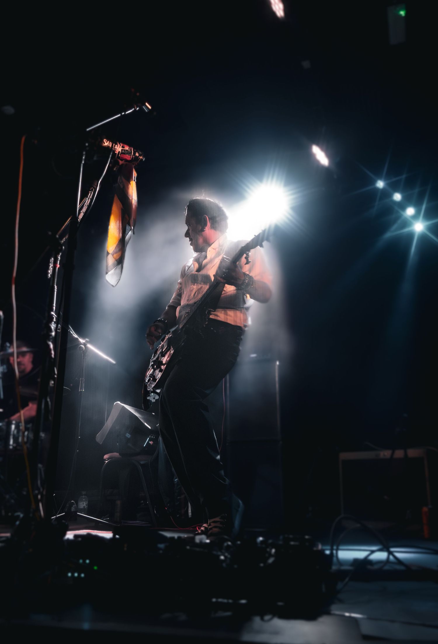 Guitarist performing on stage under dramatic spotlight with smoke effects at a live concert.