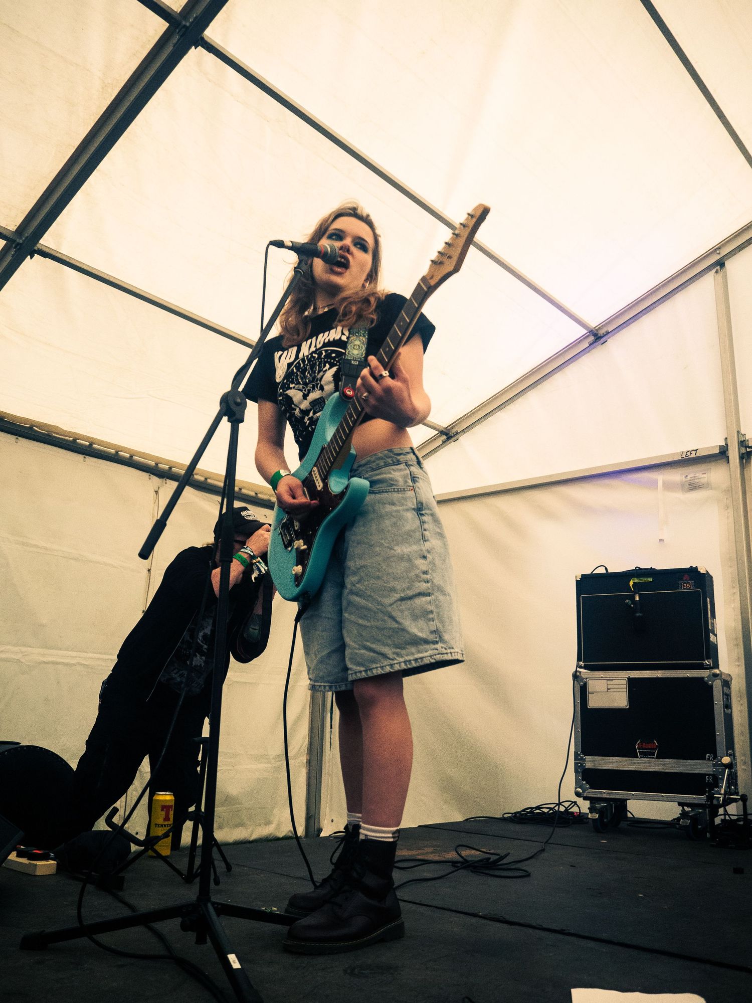 Musician playing electric guitar while singing into microphone in a festival tent setup.