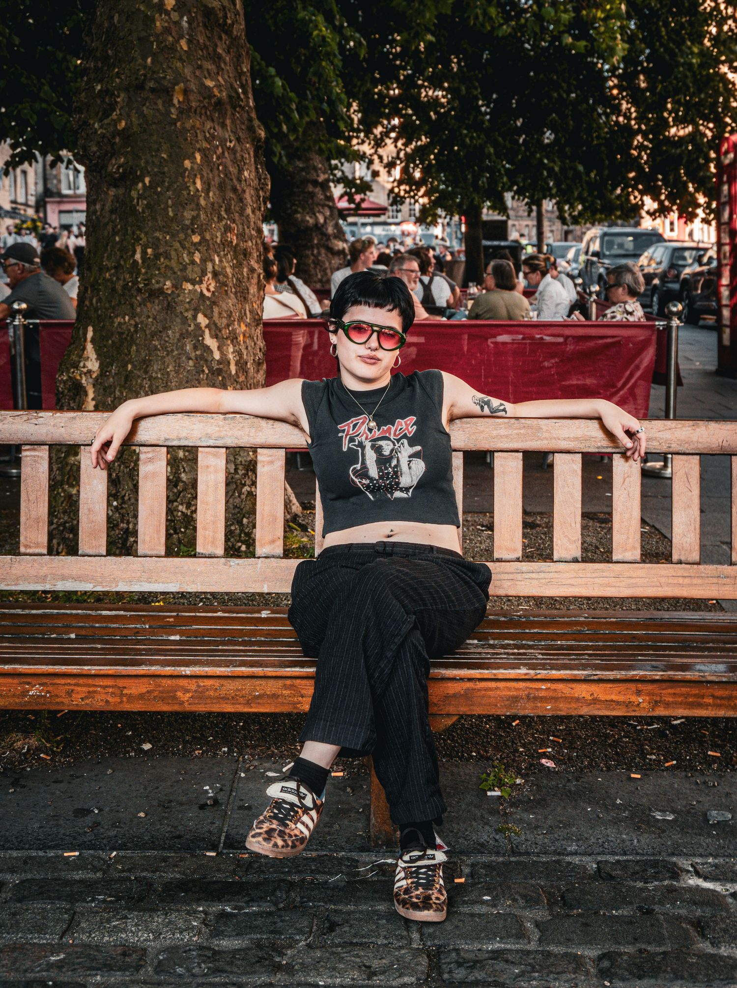 Young woman in red sunglasses relaxing on wooden park bench wearing band tee and black pants.