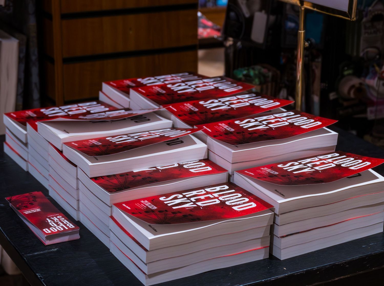 Stacks of red hardcover books displayed on a table at a bookstore or book launch event.