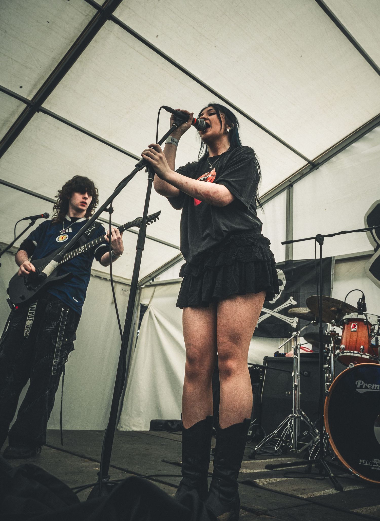 Female vocalist singing on stage with guitarist in background at live music festival.