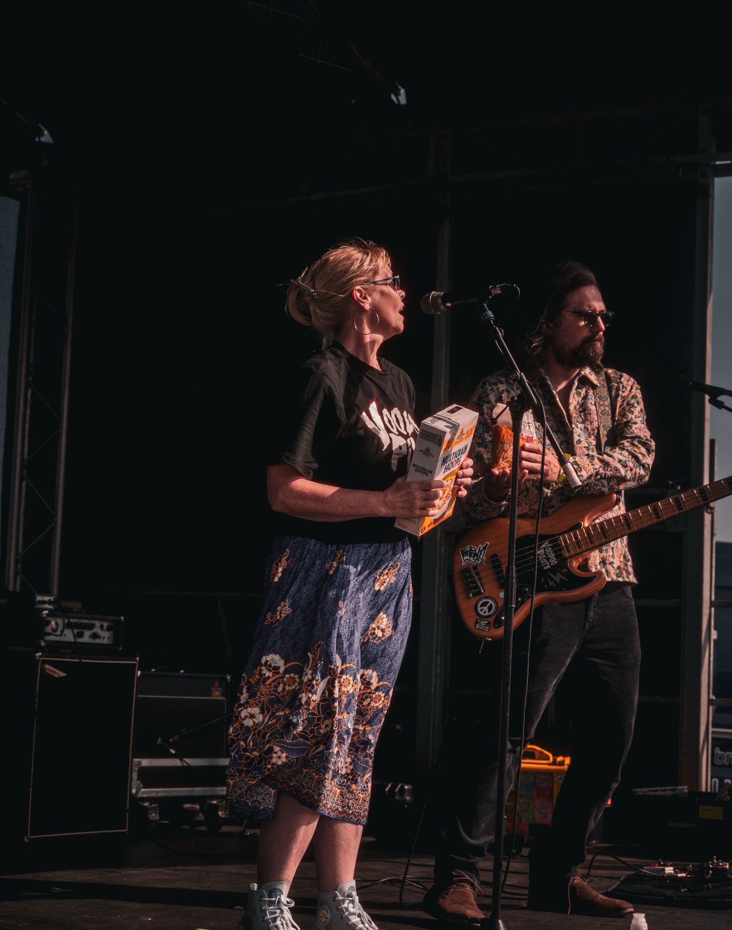 A female vocalist and male guitarist performing live on stage at an outdoor music festival.