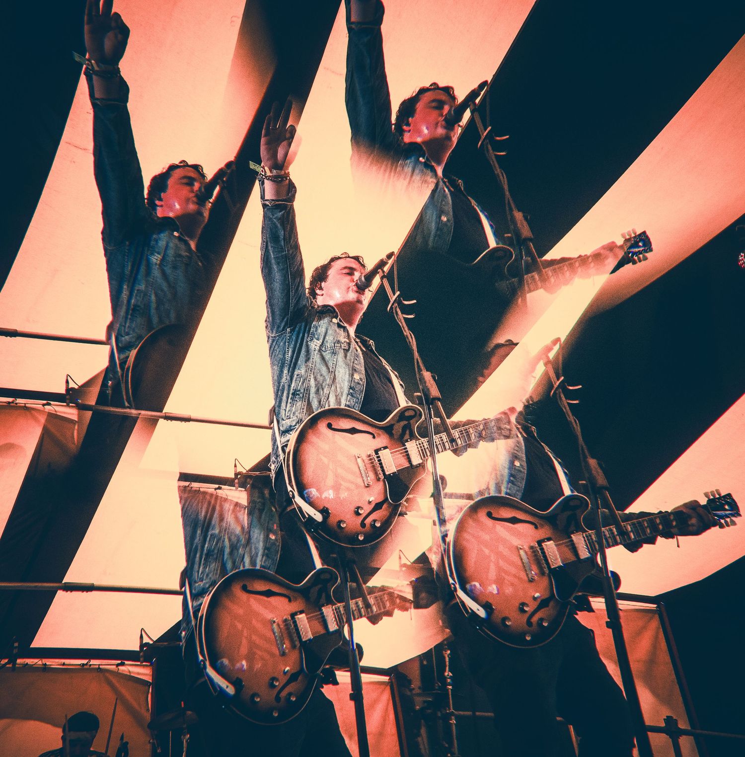 Three guitarists on stage with raised arms, bathed in warm orange light from below.