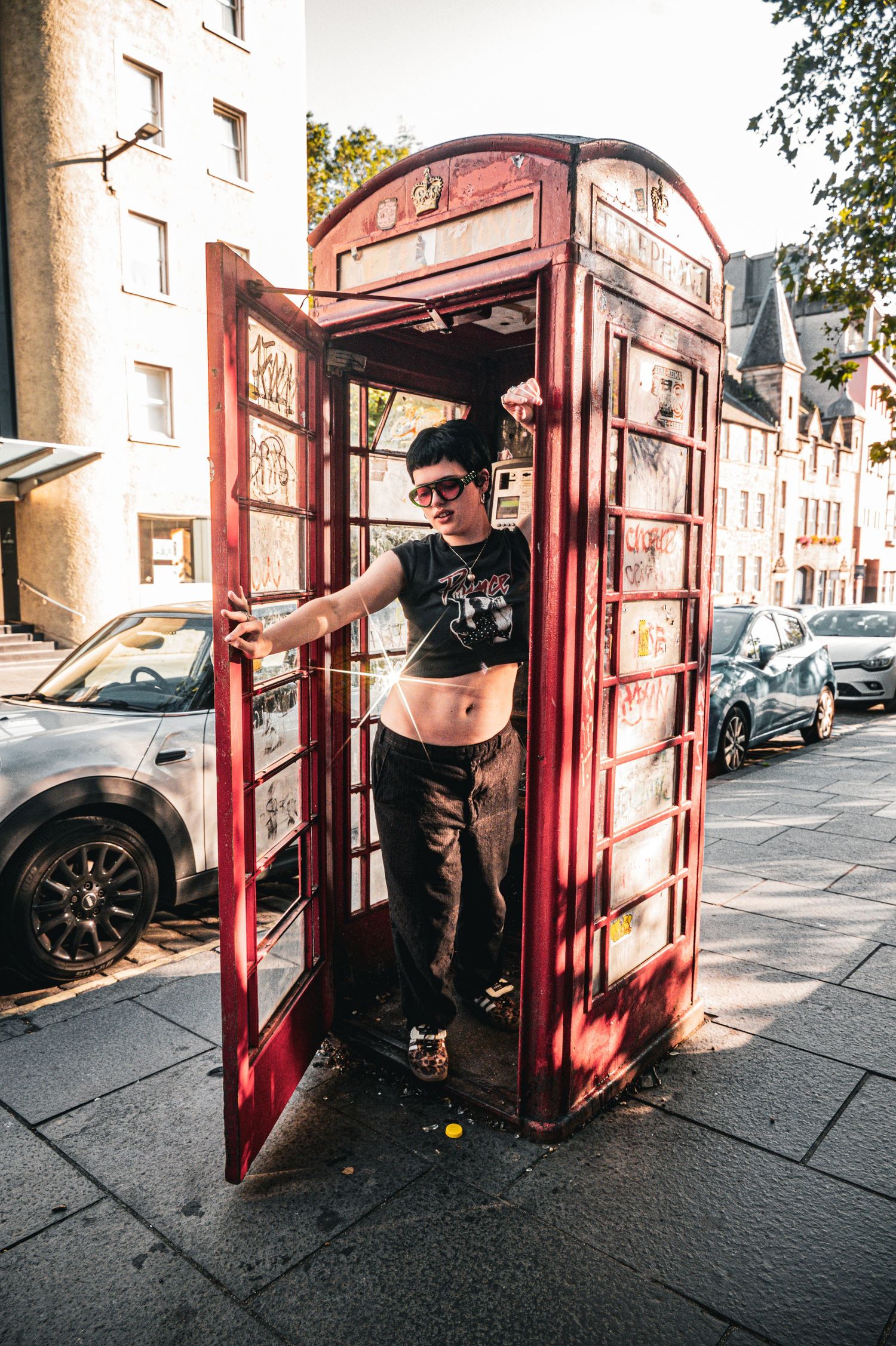 Person posing inside a vintage red British phone booth on a city street.
