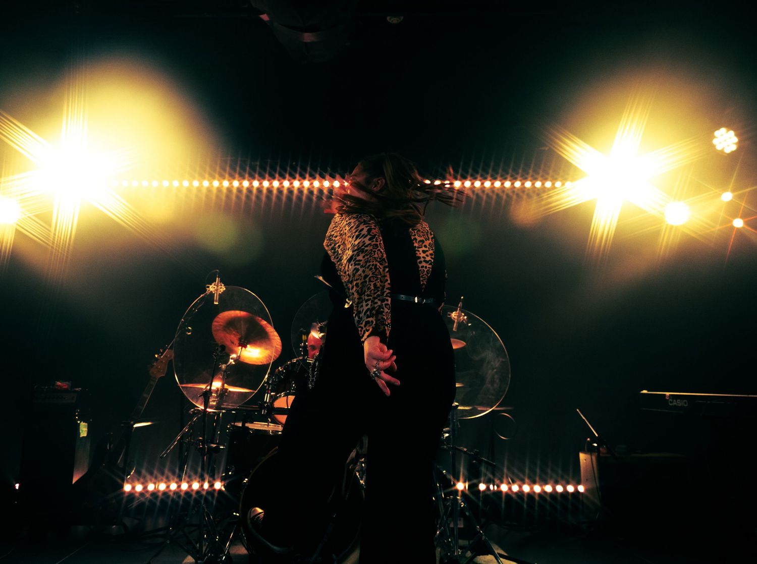 A silhouetted performer stands on stage between bright spotlights during a dramatic concert performance.