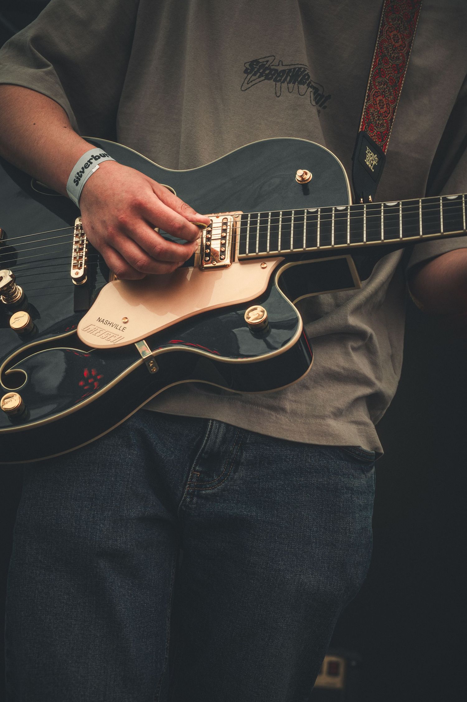 Close-up of guitarist playing black Gretsch Nashville electric guitar with decorative red strap.