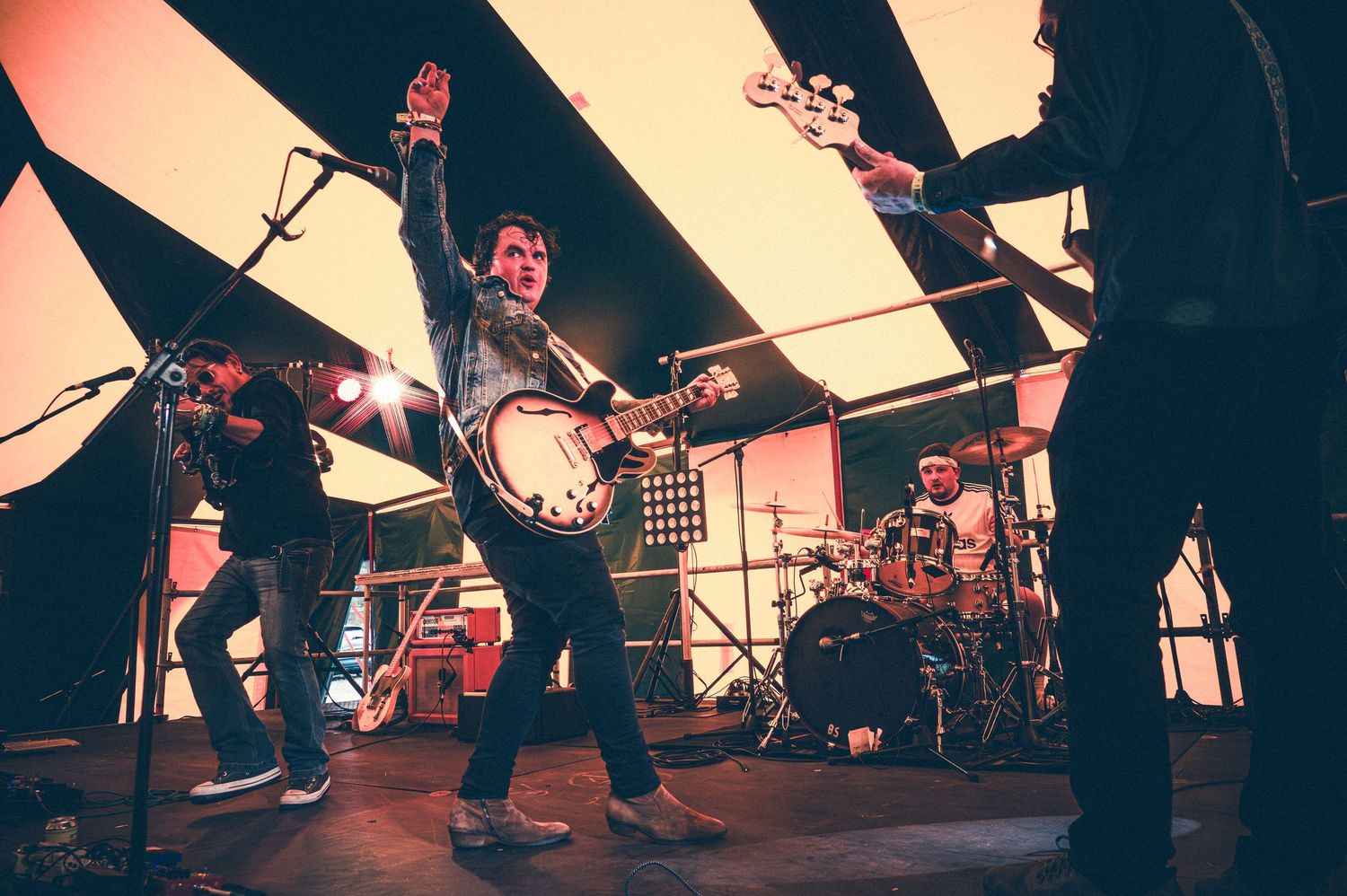 Rock band performing energetically on stage with guitarist, drummer, and vocalist under dramatic lighting.