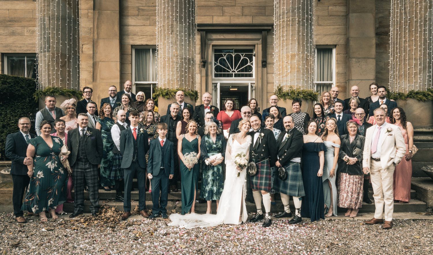 Large wedding party group photo outside grand stone Scottish country house venue.