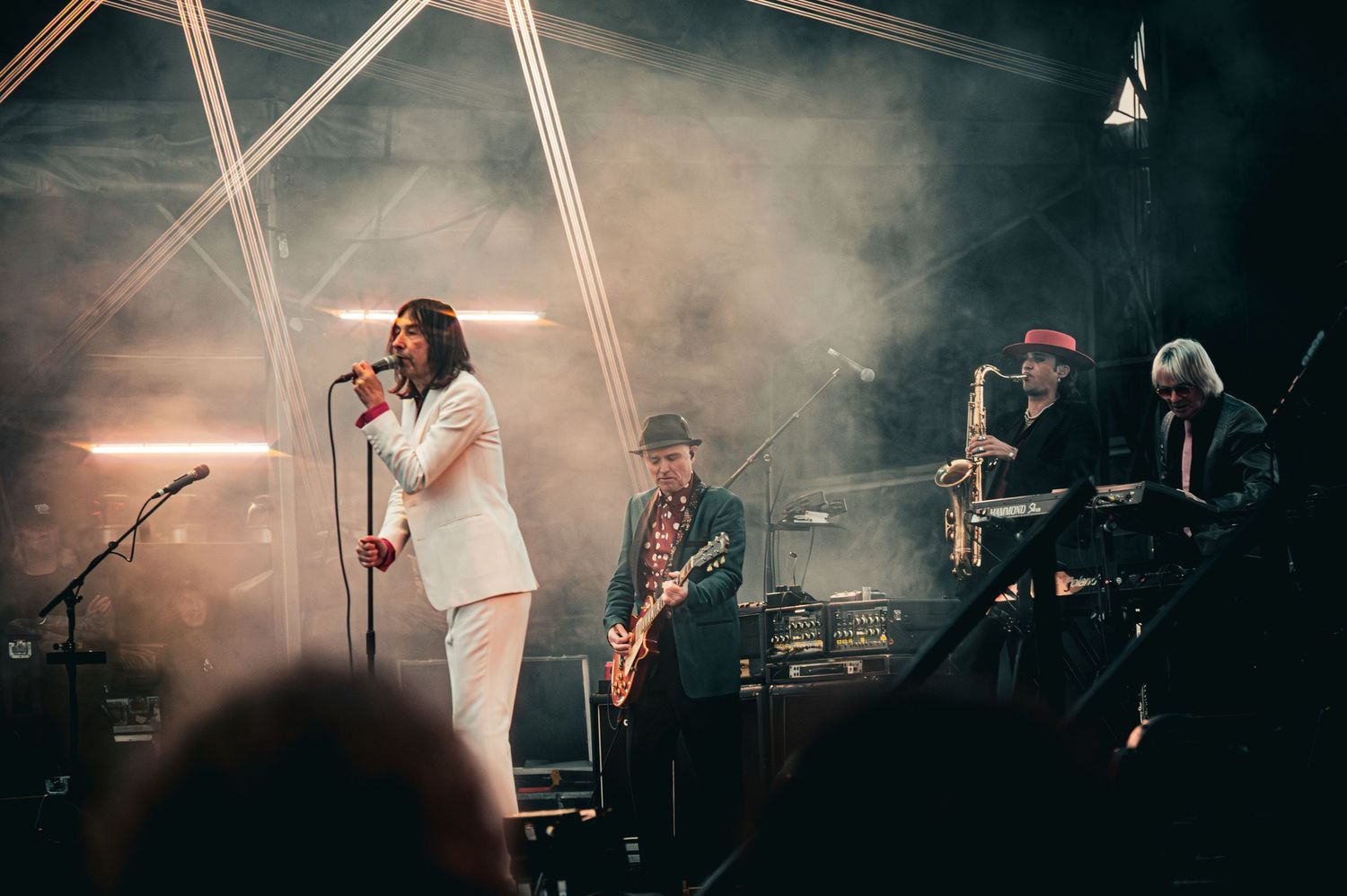 Live band performs on smoky stage, featuring a female vocalist in white suit, guitarist, saxophonist, and keyboardist.