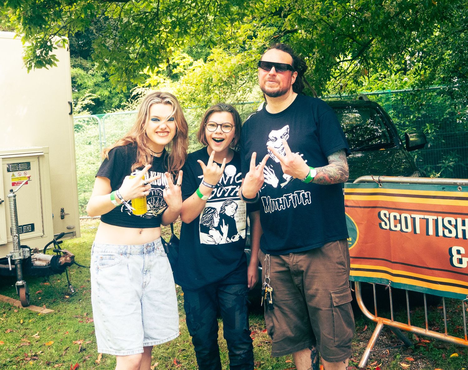 Three friends posing together outdoors near a Scottish-themed trailer.
