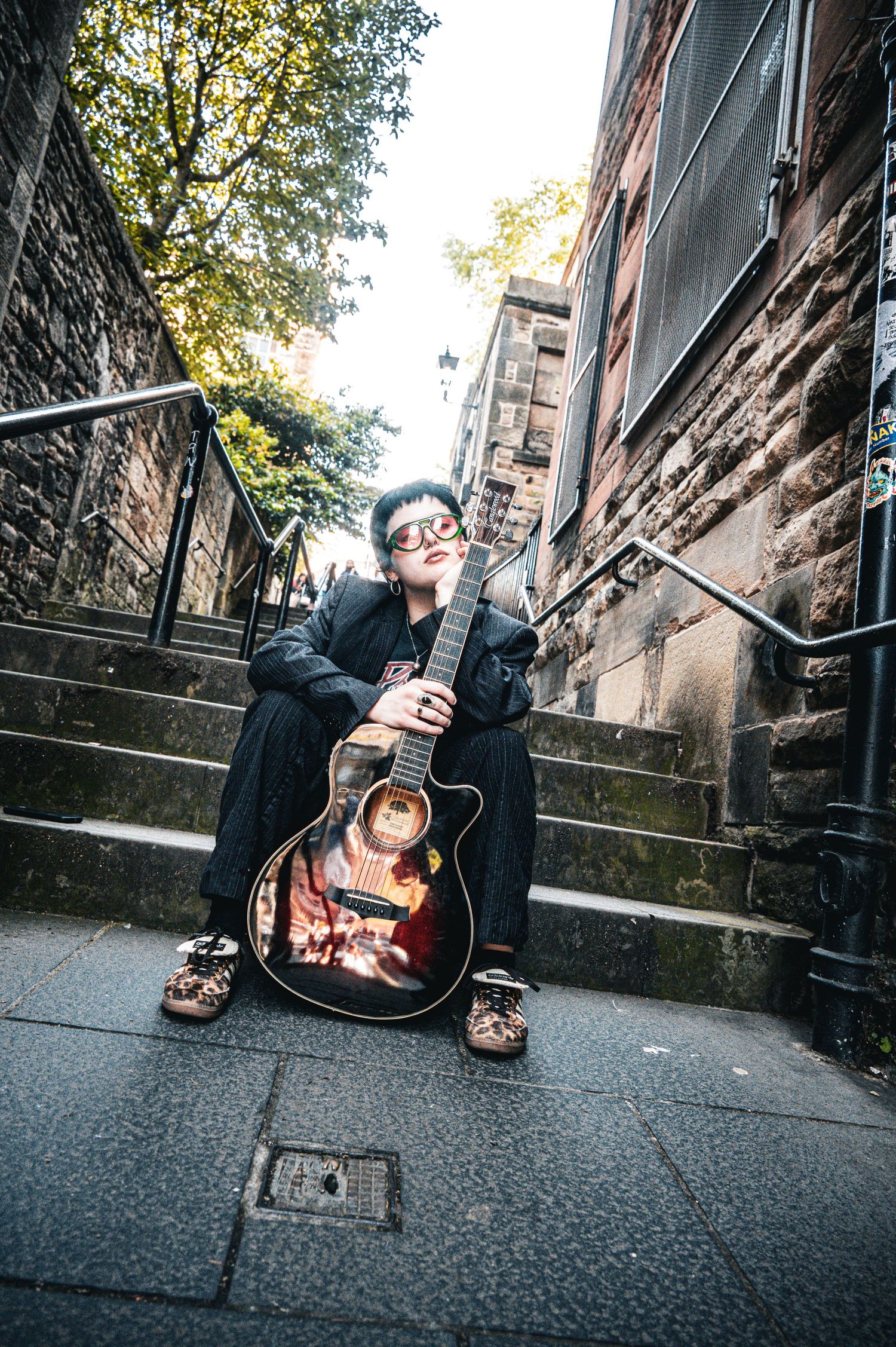 Person sitting on steps holding a decorative acoustic guitar in an urban alleyway setting.