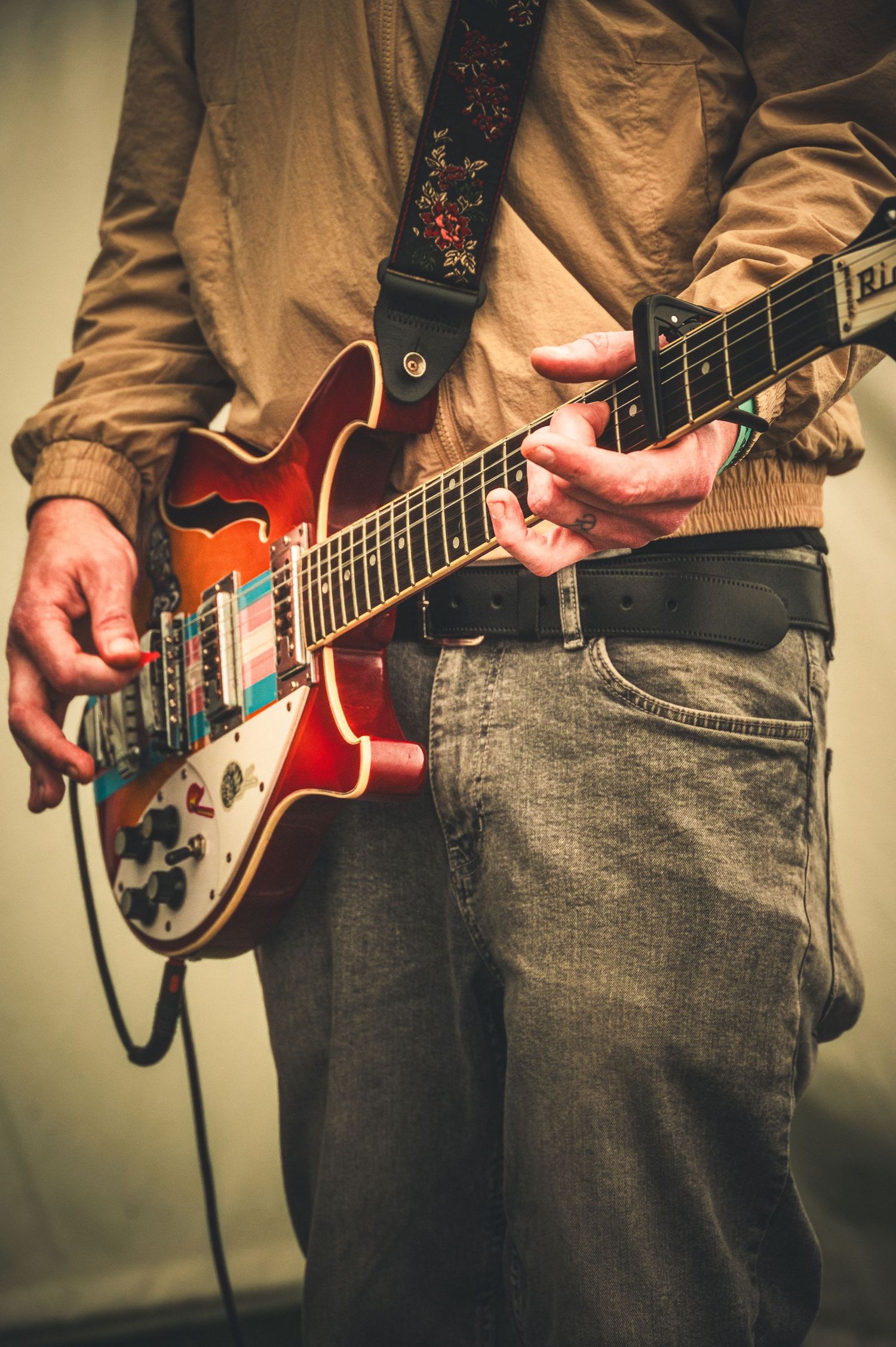 Close-up of musician playing vintage semi-hollow electric guitar with decorative strap.
