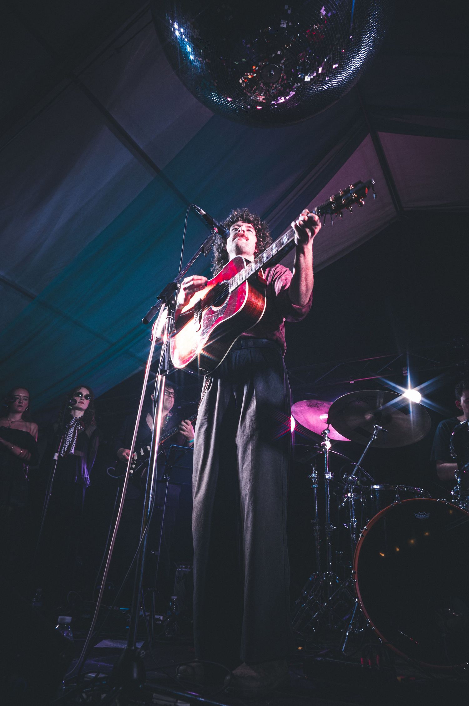 Musician playing red guitar on stage under disco ball with dramatic lighting at live concert.