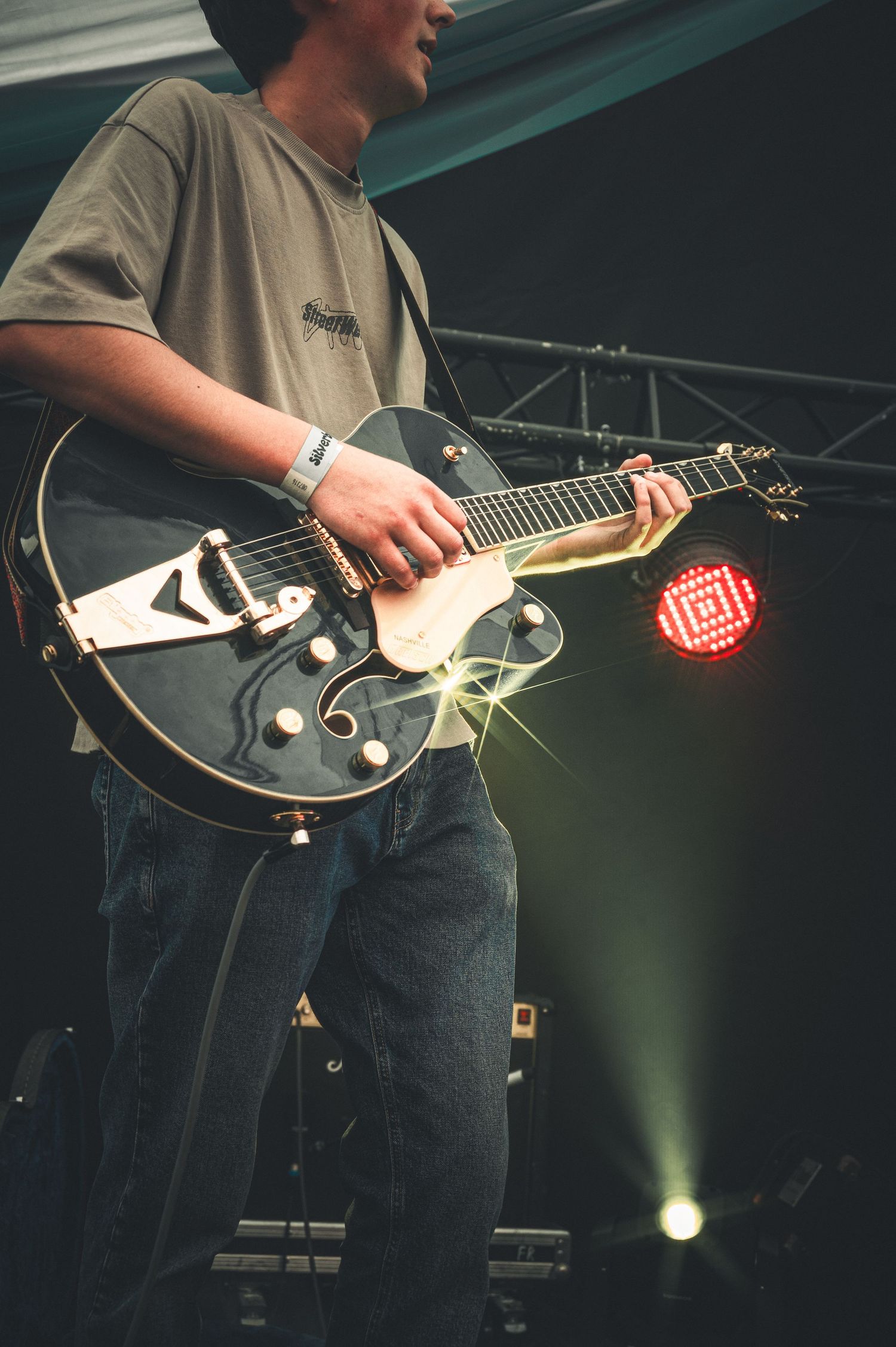 Musician playing a black Gretsch hollow-body electric guitar on stage under red and white concert lights.