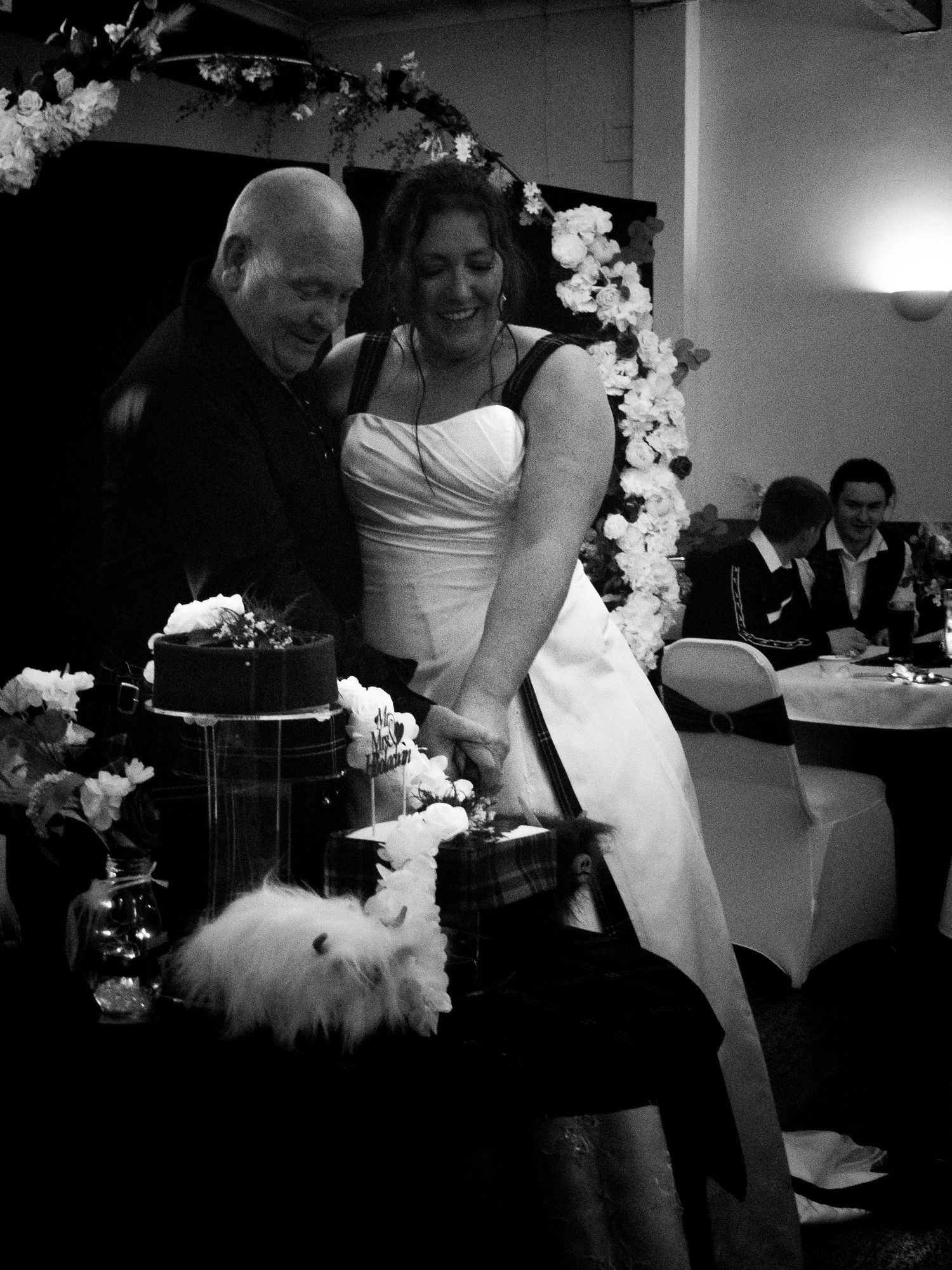 Bride and groom smiling while cutting their wedding cake together, surrounded by floral decorations.