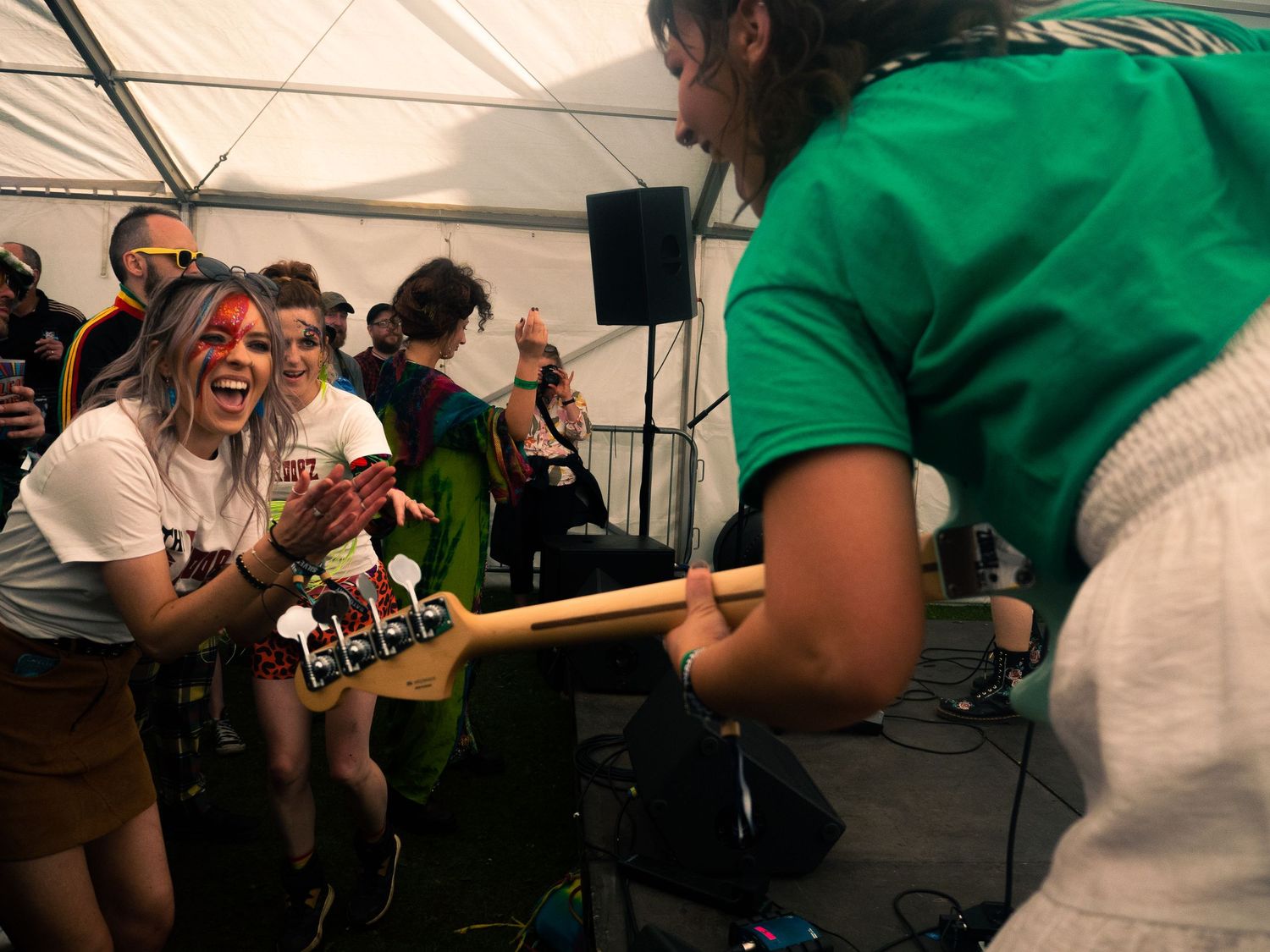 Musicians jamming together with guitars during an animated performance under tent.