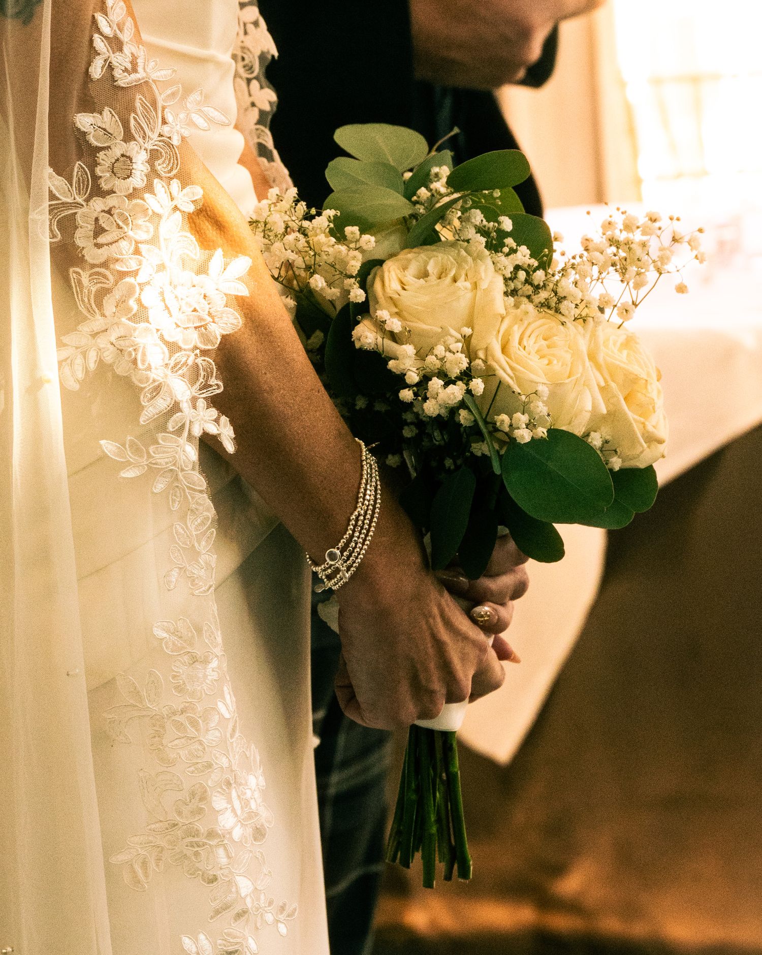 Close-up of bride and groom holding a white rose and baby's breath wedding bouquet together.