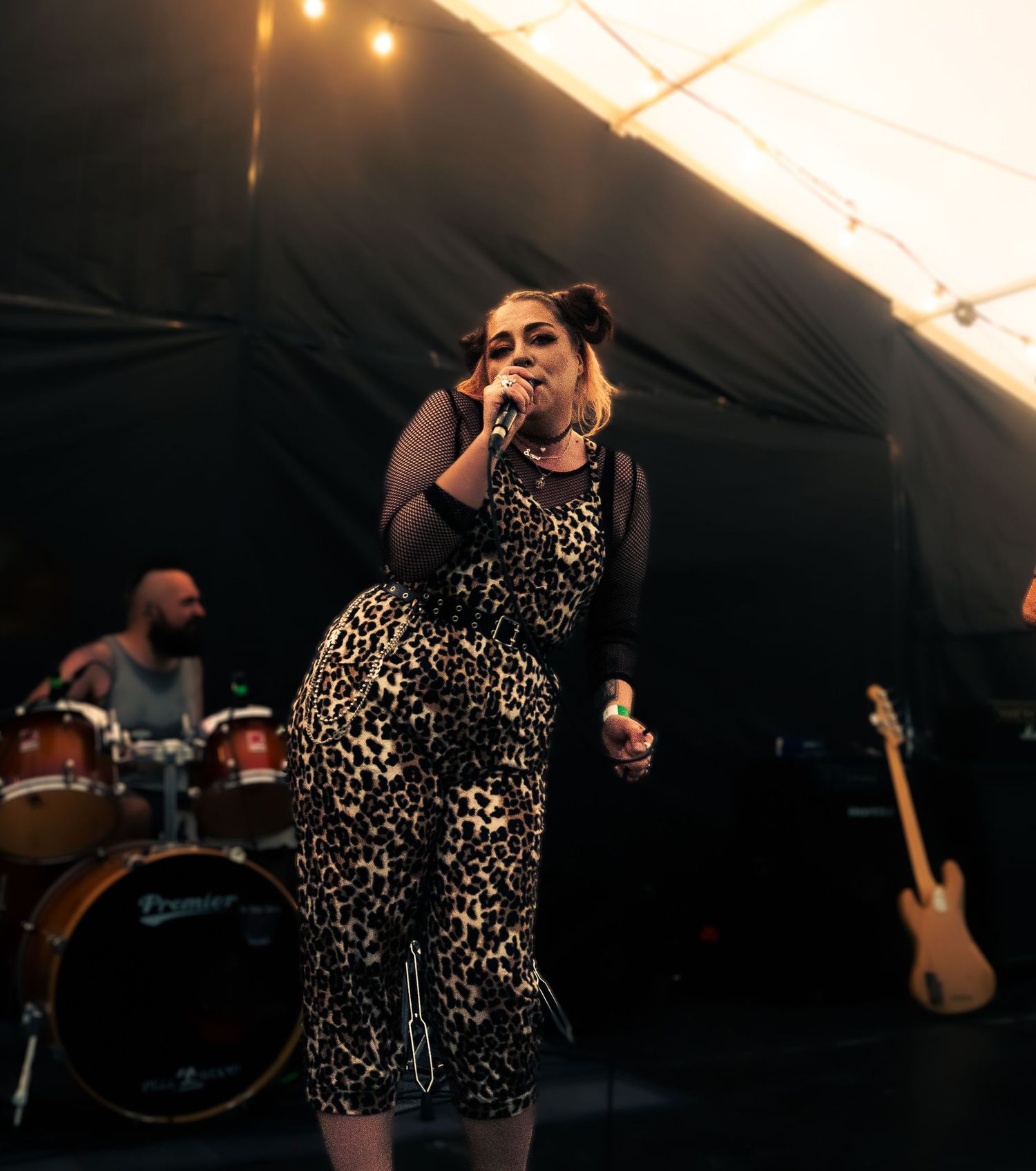 Singer performs in leopard print outfit under tent lighting at outdoor music festival.