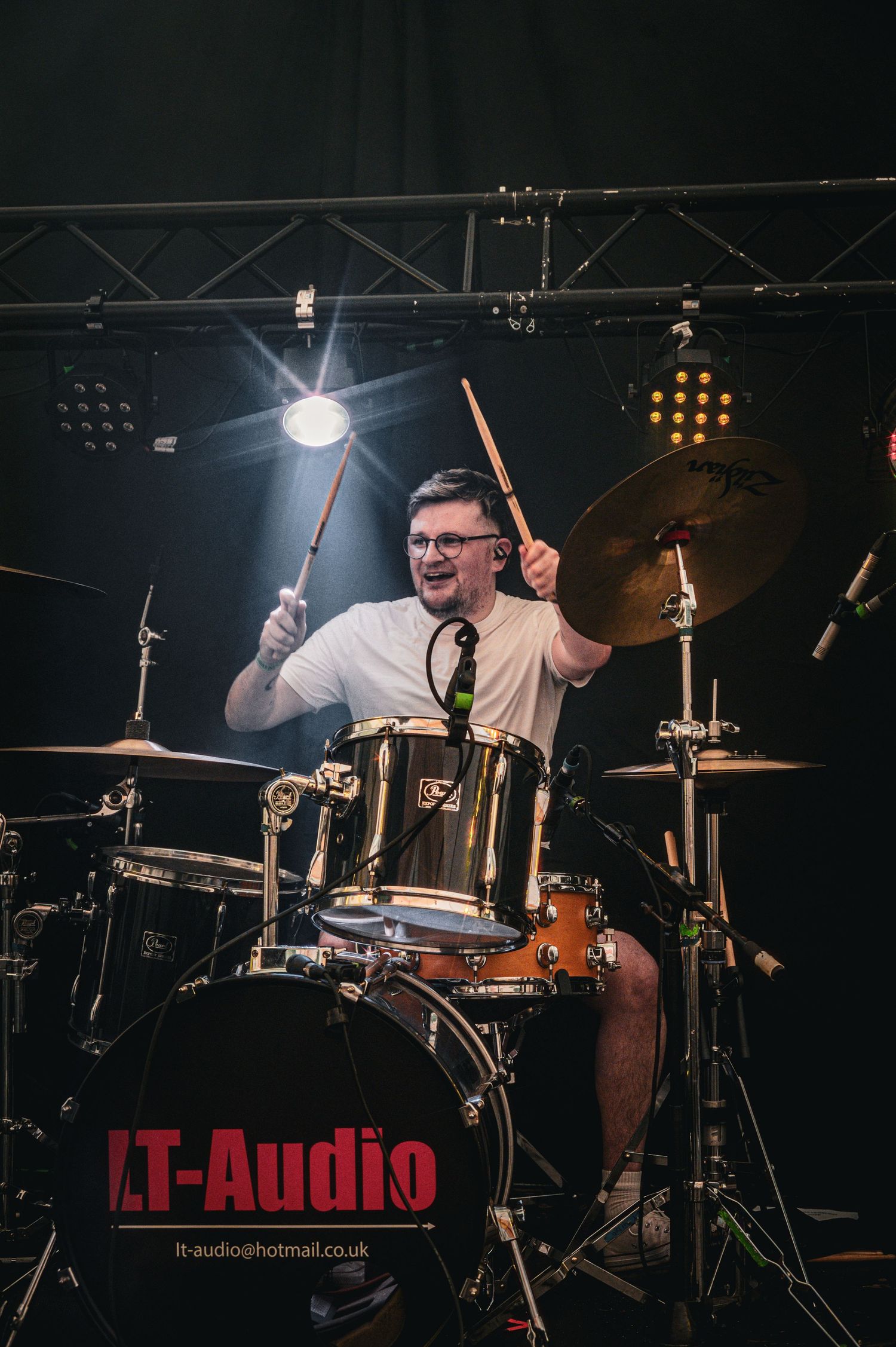 Energetic drummer playing Zildjian cymbals on stage under spotlight at LT-Audio live music event.
