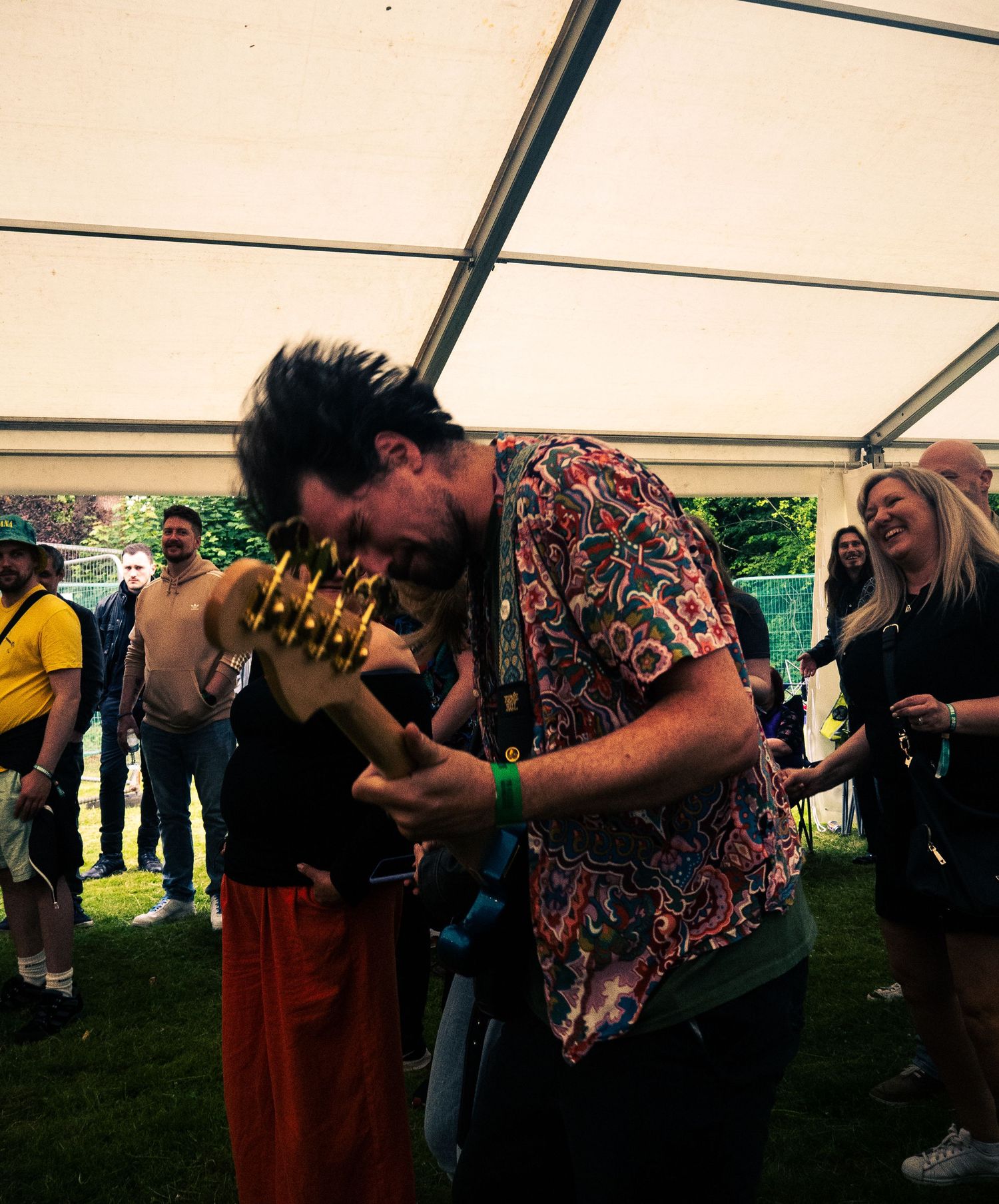 Musician playing electric guitar with passion under a white tent at an outdoor festival.