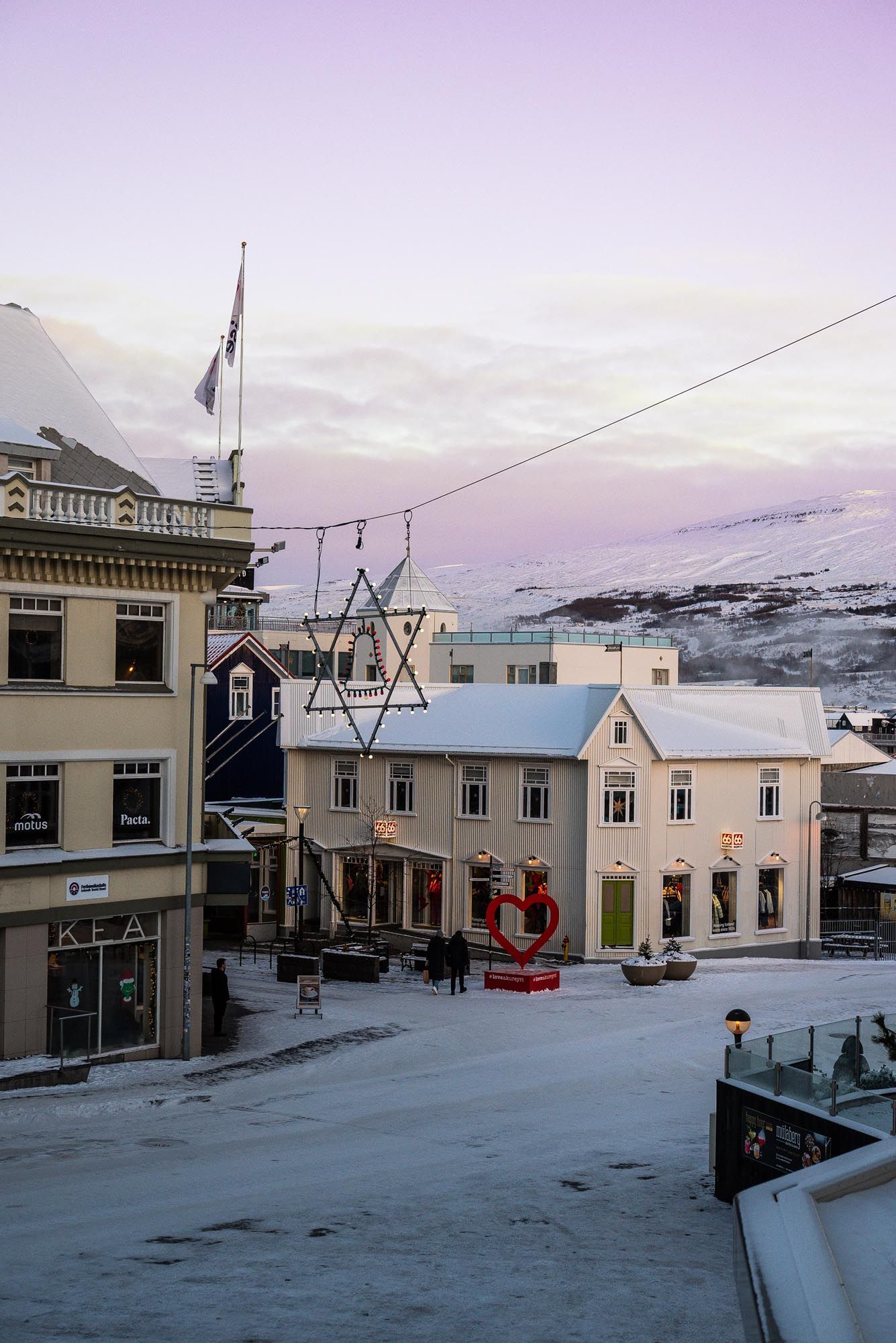 Snow-covered street in Akureyri, Iceland with historic buildings and a purple winter sunset sky in the background.