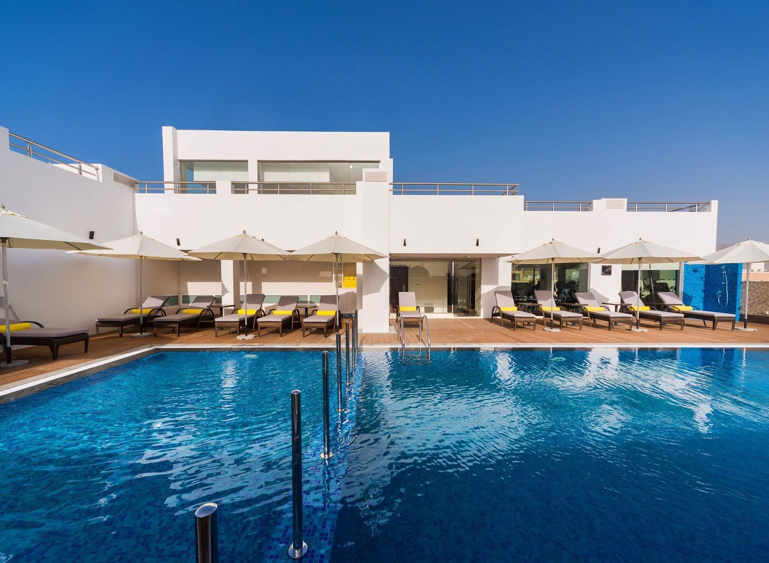 A luxurious rooftop infinity pool with white architecture and lounge chairs overlooking a bright blue sky.