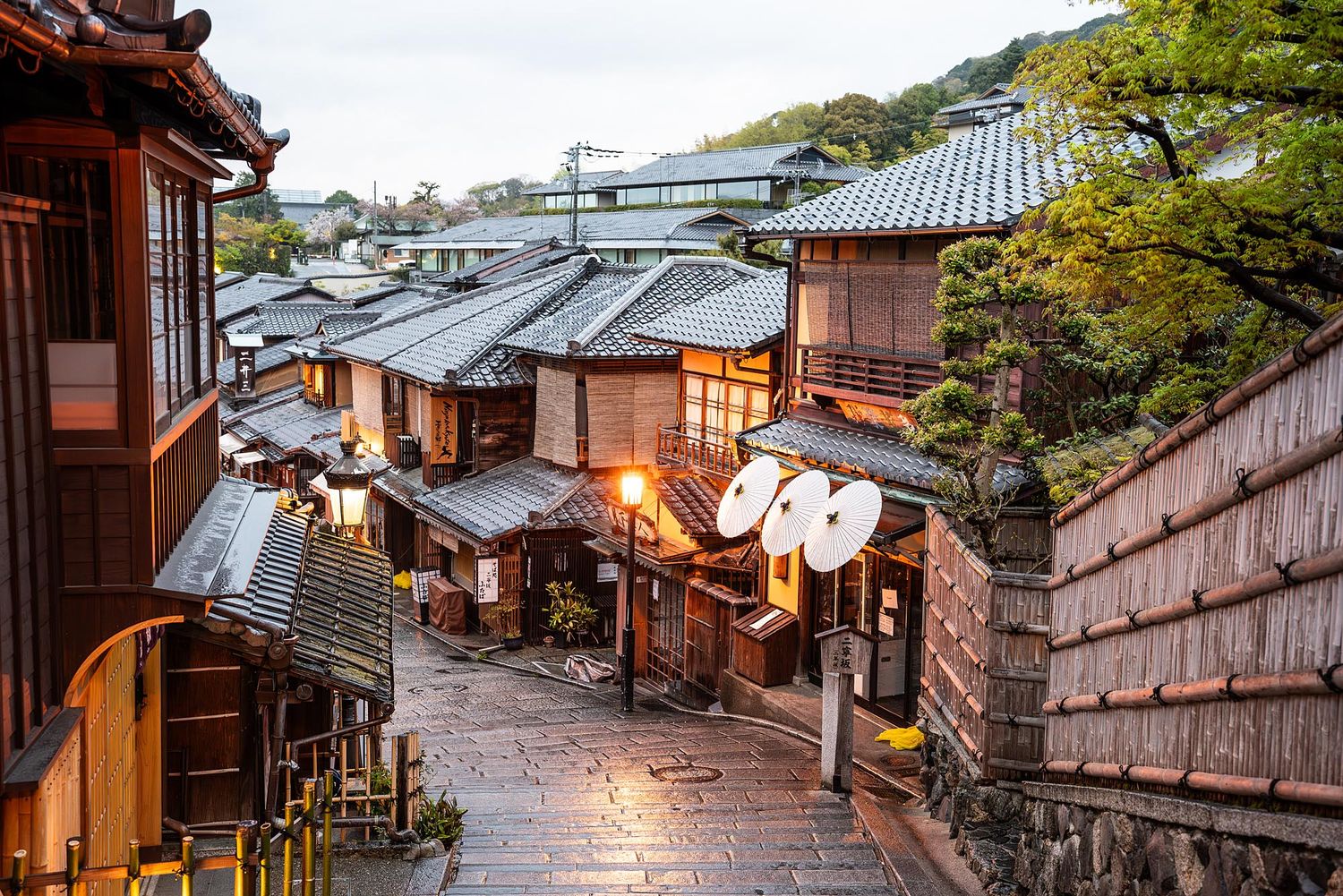 Traditional wooden buildings line a narrow cobblestone street in the historic Higashiyama district of Kyoto at dusk.