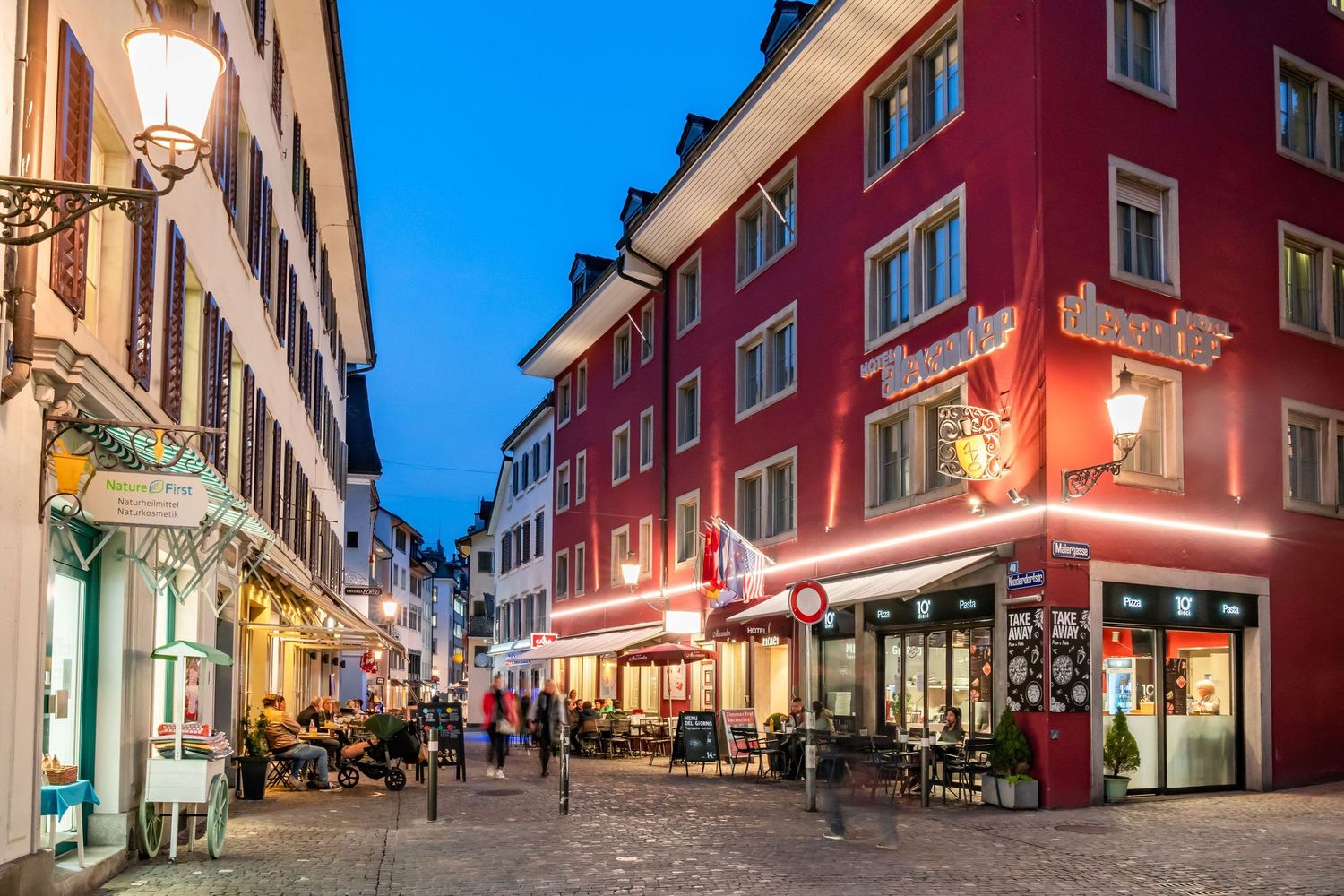 Illuminated cobblestone street with red buildings and shops at dusk in a charming European town.