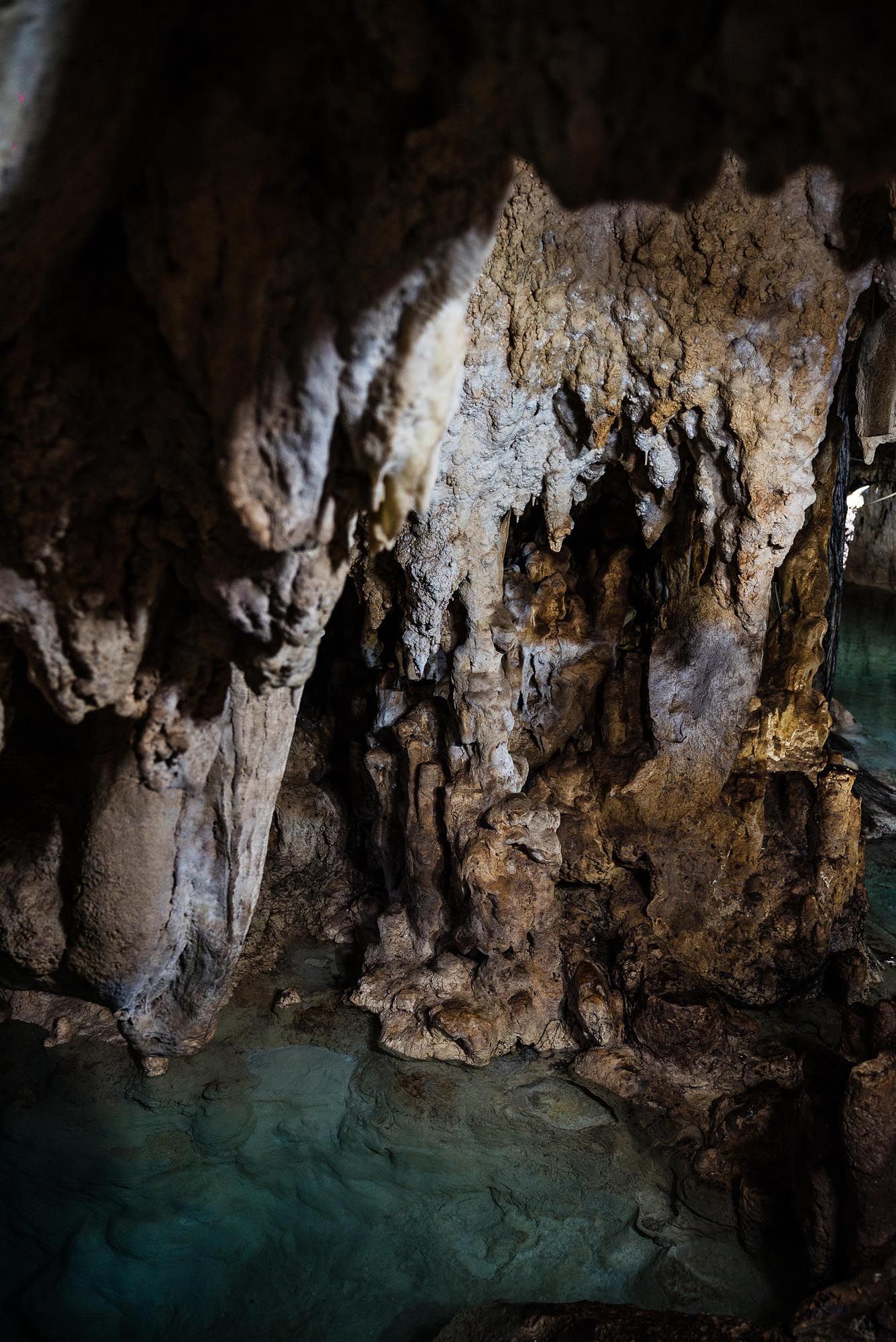 Dark limestone cave formations reflect on turquoise underground water in a natural cavern system.