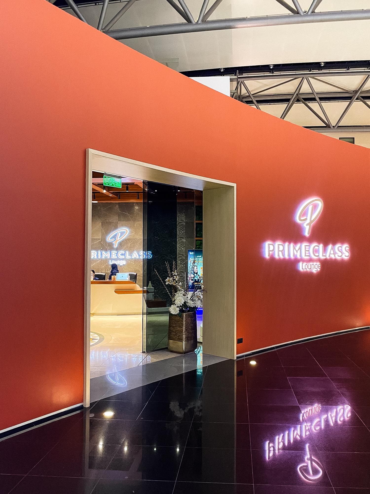 Neon pink 'Flying Class' sign illuminates a dark corridor with orange walls and reflective black flooring.