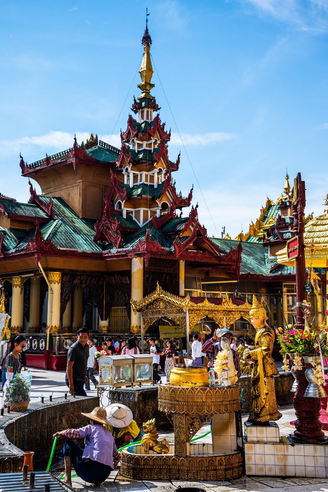 Ornate Buddhist temple complex with traditional Burmese architecture and golden spires against blue sky at Shwedagon Pagoda.