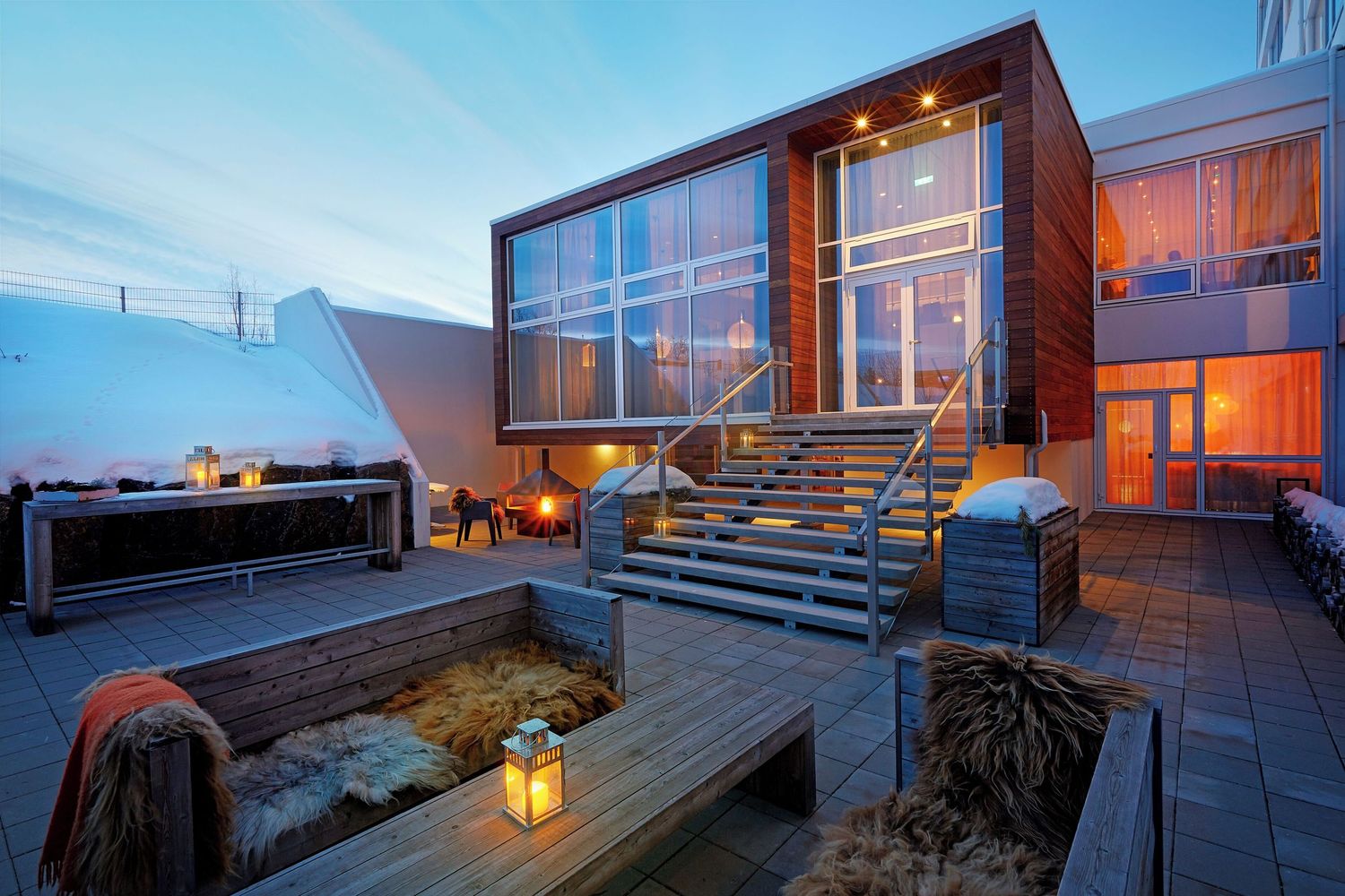 A modern oceanfront deck with glowing lanterns and wooden furniture at twilight overlooking the sea.