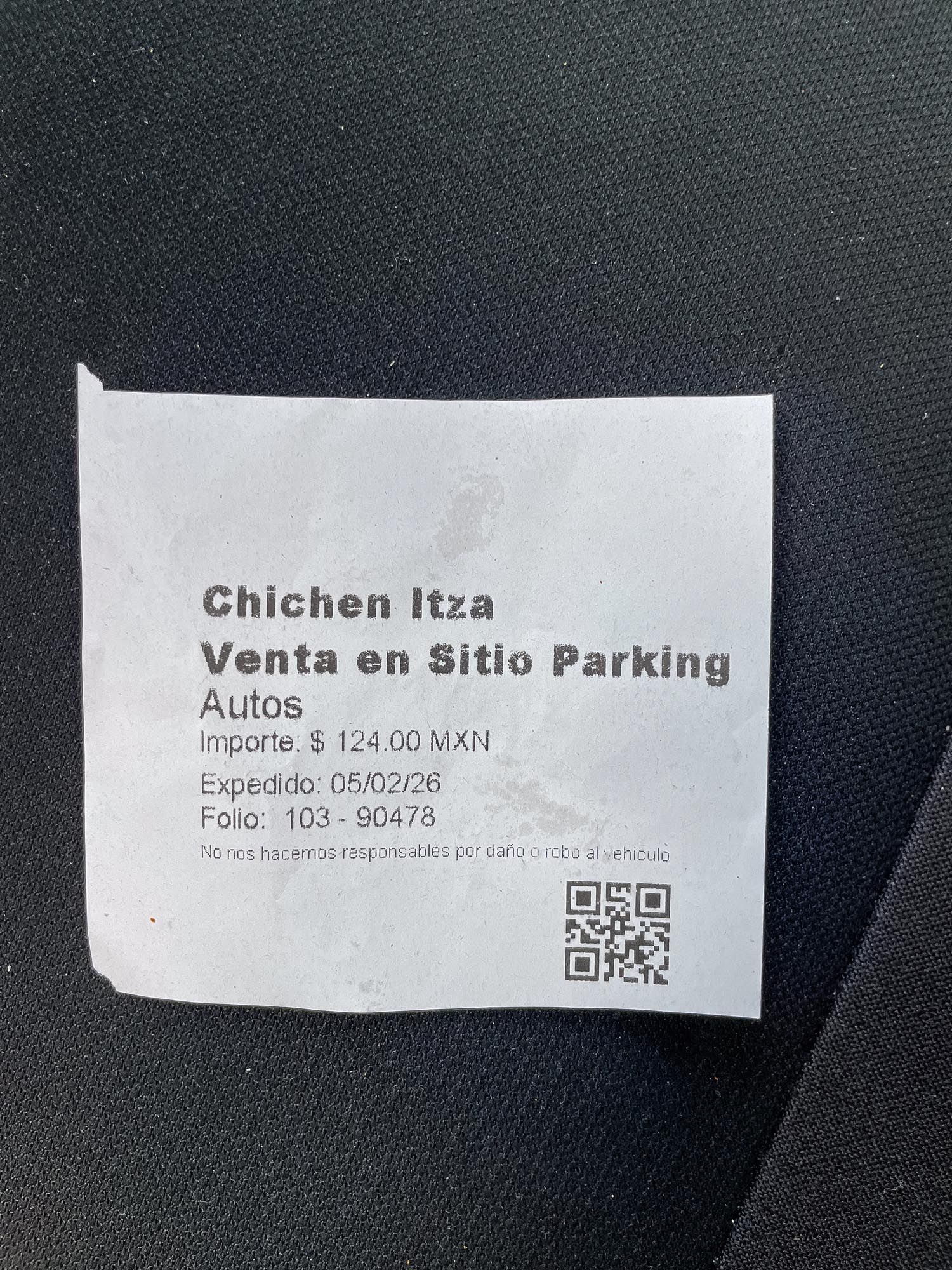 Close-up view of paper tickets and QR codes for Chichen Itza admission and parking displayed on a dark surface.
