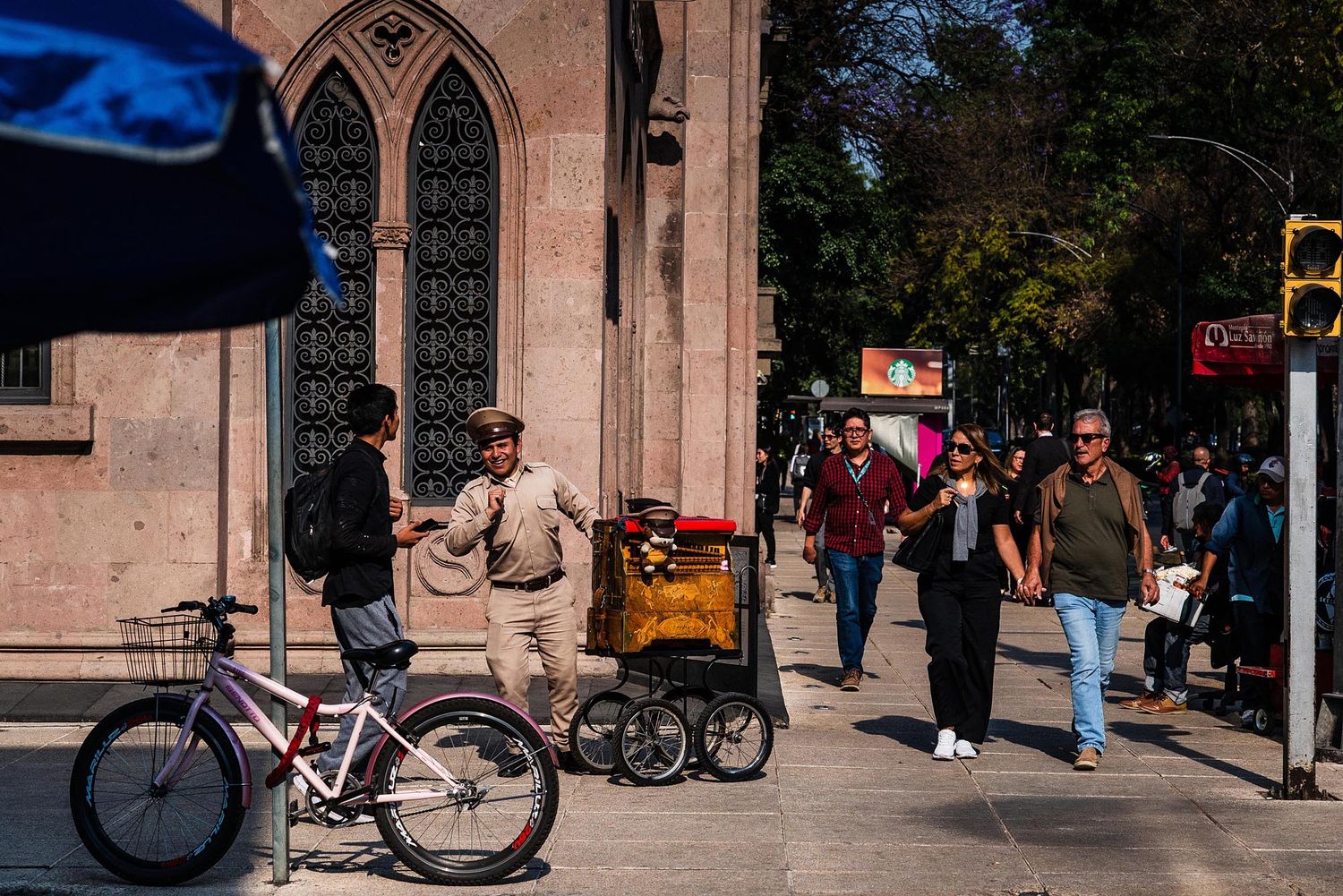 A row of bicycles parked outside a brick building with pedestrians walking on a sunny day.