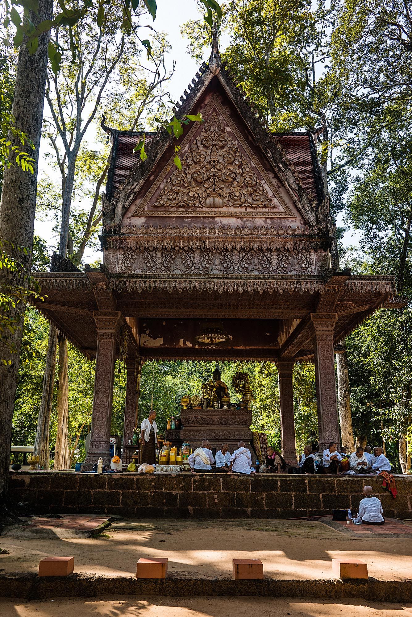 Traditional wooden Thai pavilions with ornate roofs stand in a peaceful forest setting at Prasat Muang Tam temple complex.