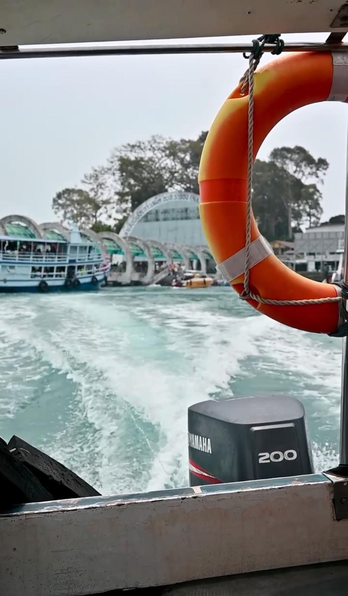 Wake from boat motor churns up turquoise waters near coastal houses as seen from rear of vessel.