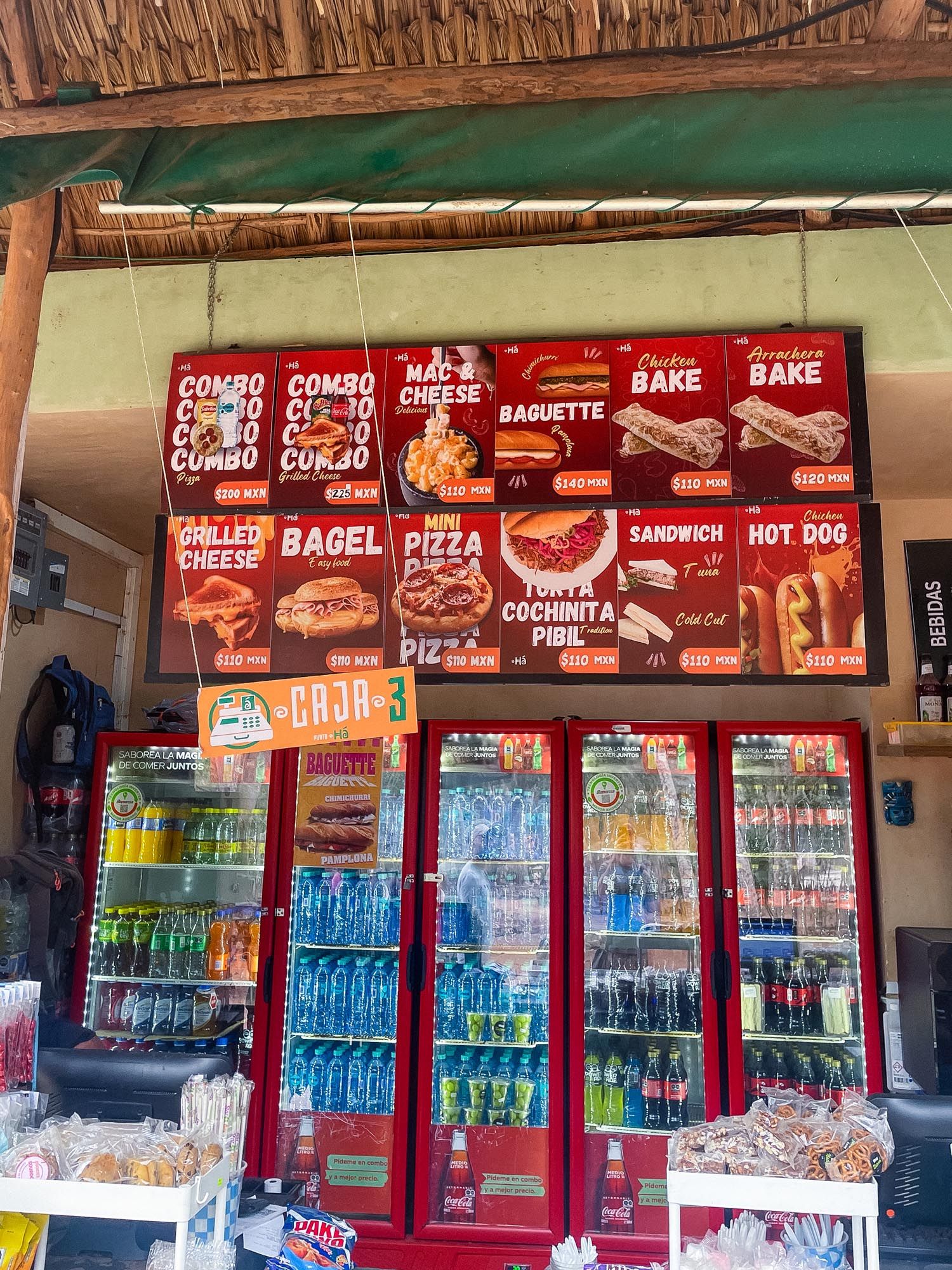 Row of commercial refrigerators with red trim displaying beverages in a convenience store with menu boards above.
