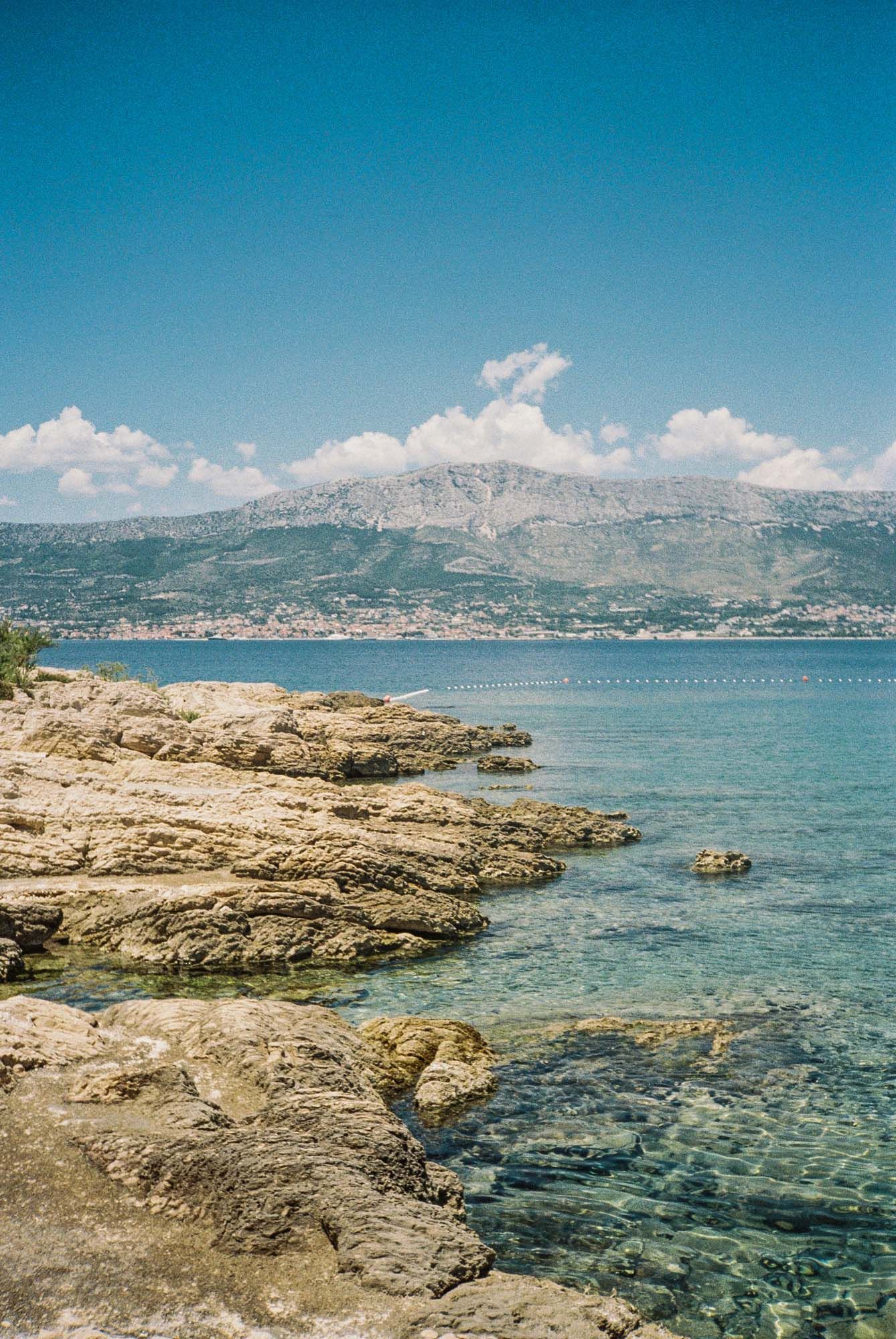 Rocky coastline with crystal clear turquoise waters and mountains in the background along the Mediterranean Sea.