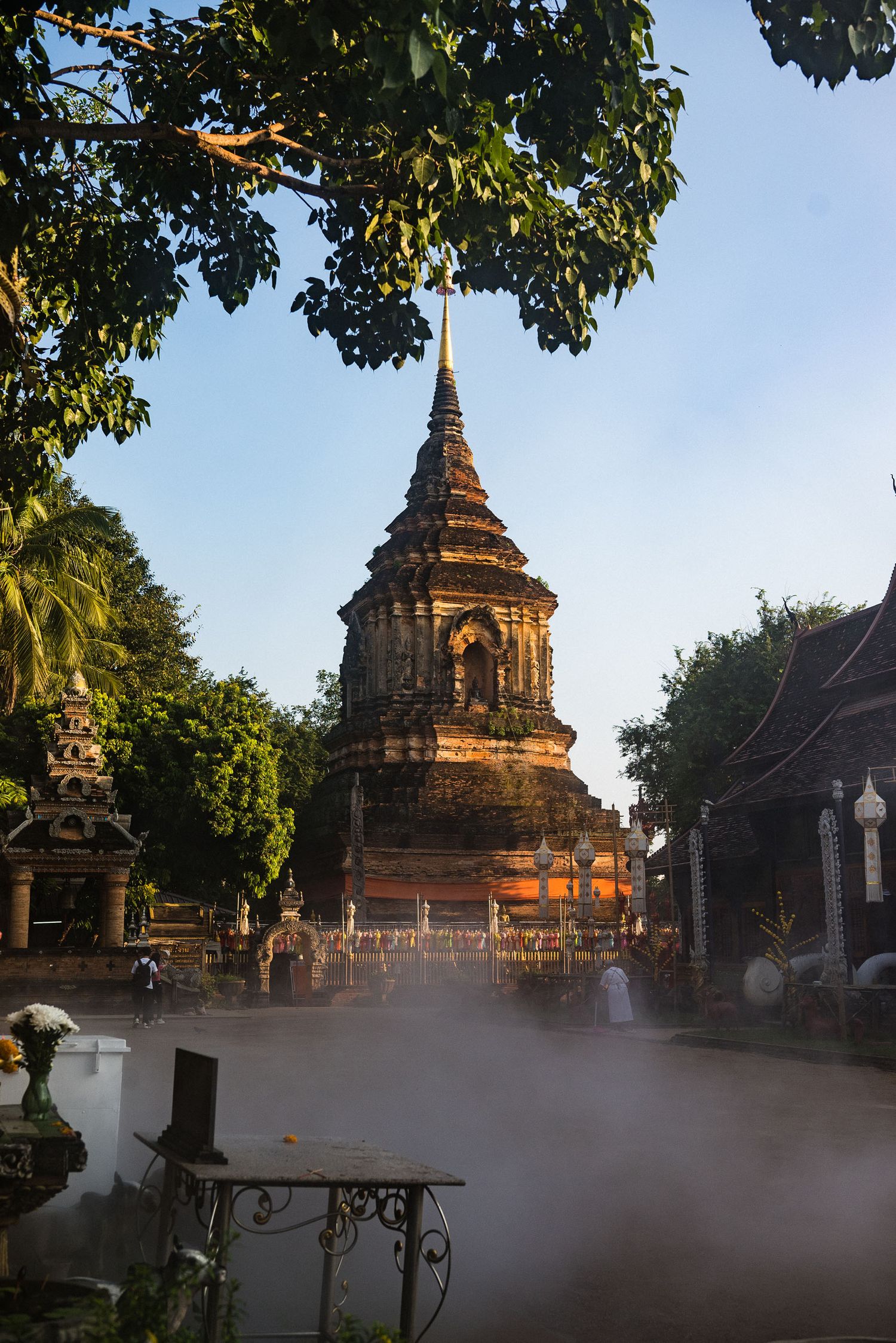 Ancient Buddhist temple stupa with ornate architecture surrounded by morning mist and tropical foliage in Thailand.