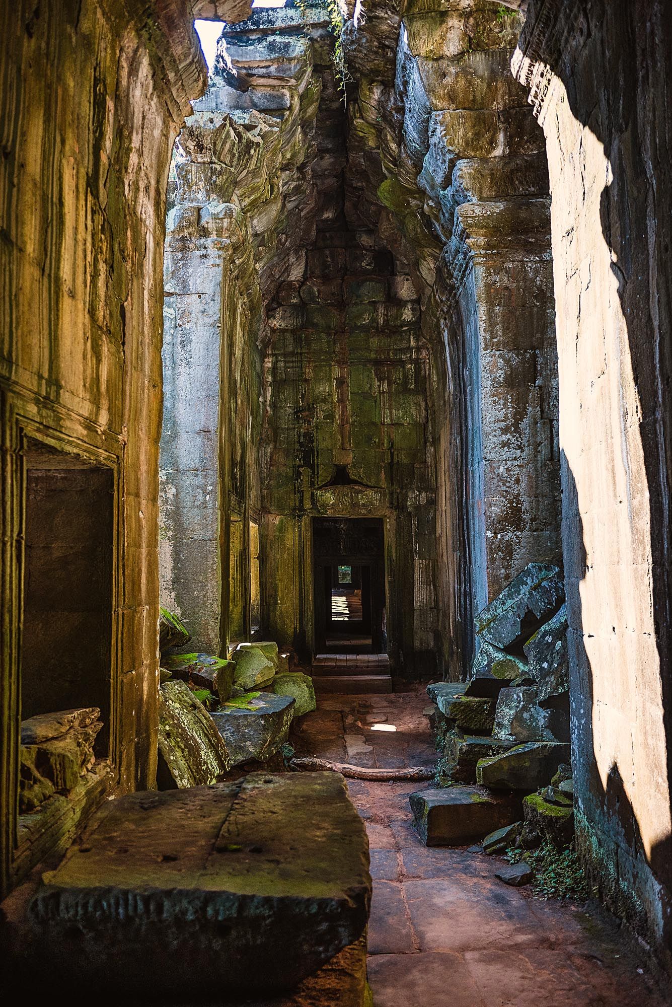 Ancient stone corridors of Angkor Wat temple complex with sunlight streaming through openings and moss-covered walls.