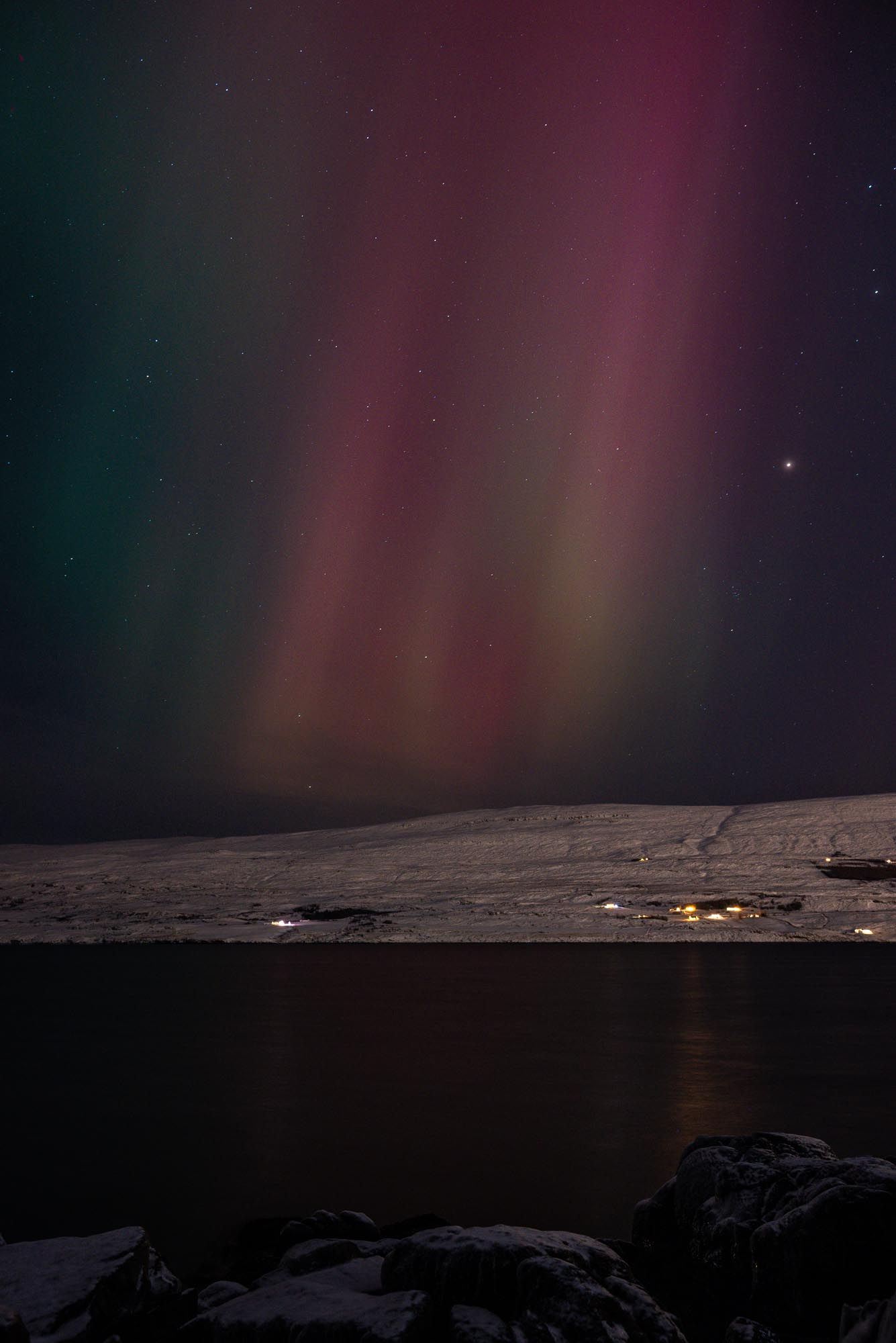 Stunning aurora borealis lights up the dark night sky over a snowy mountain landscape in vibrant pink and green hues.