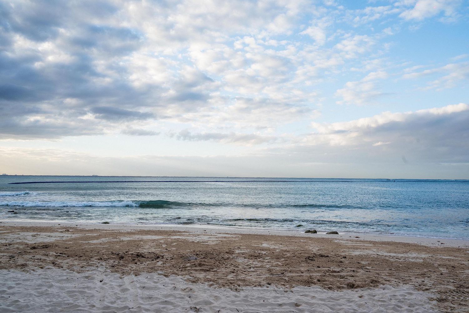 A scenic coastal beach panorama with cloudy skies and gentle waves rolling onto the sandy shore.