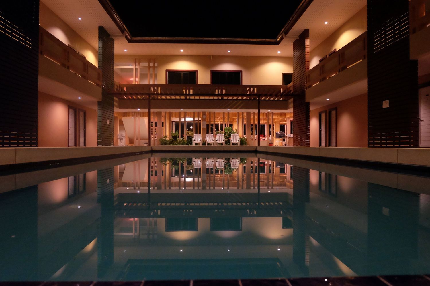 Indoor swimming pool with ambient lighting and modern architectural design features sleek columns and reflective water surface.